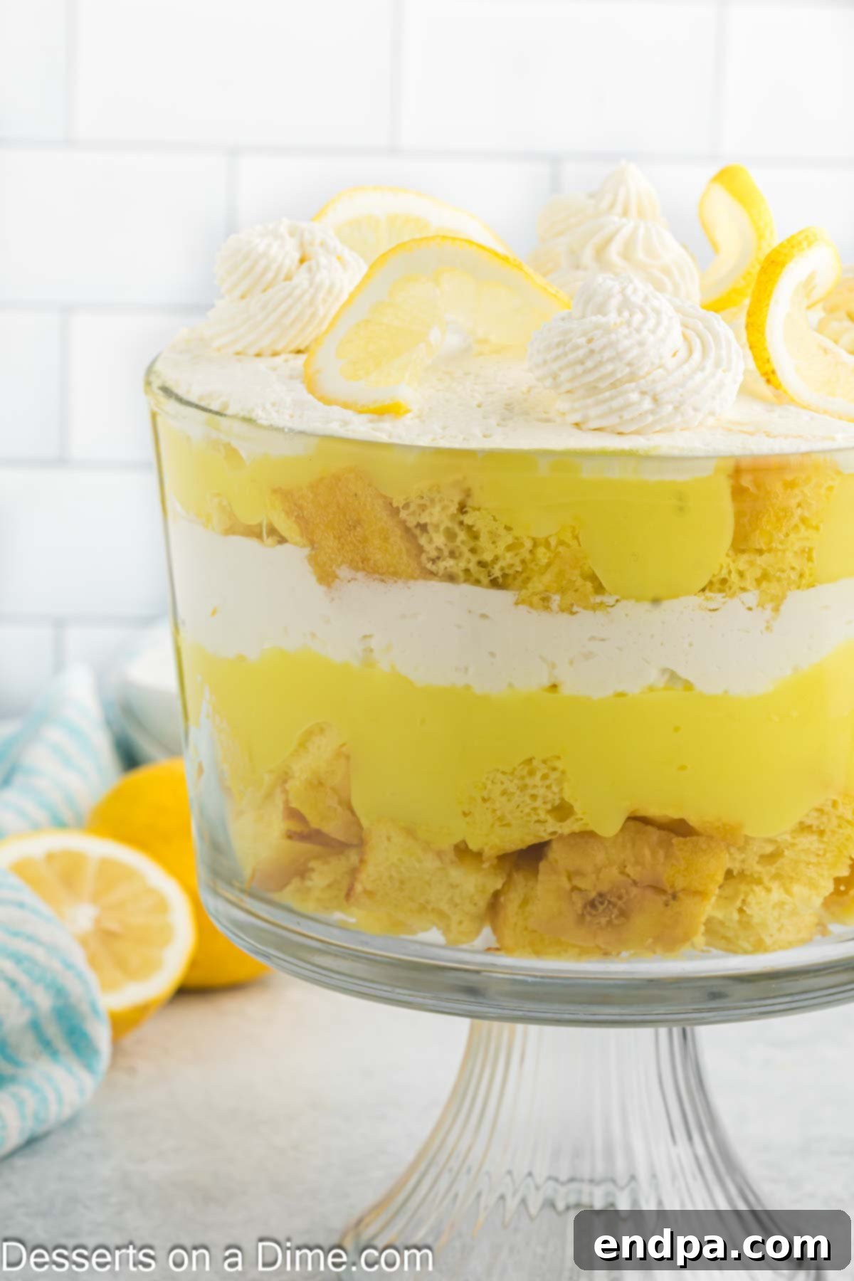 A close-up side view of a lemon trifle, showing the distinct layers of lemon cake, creamy pudding, and whipped topping, garnished with a single lemon slice.