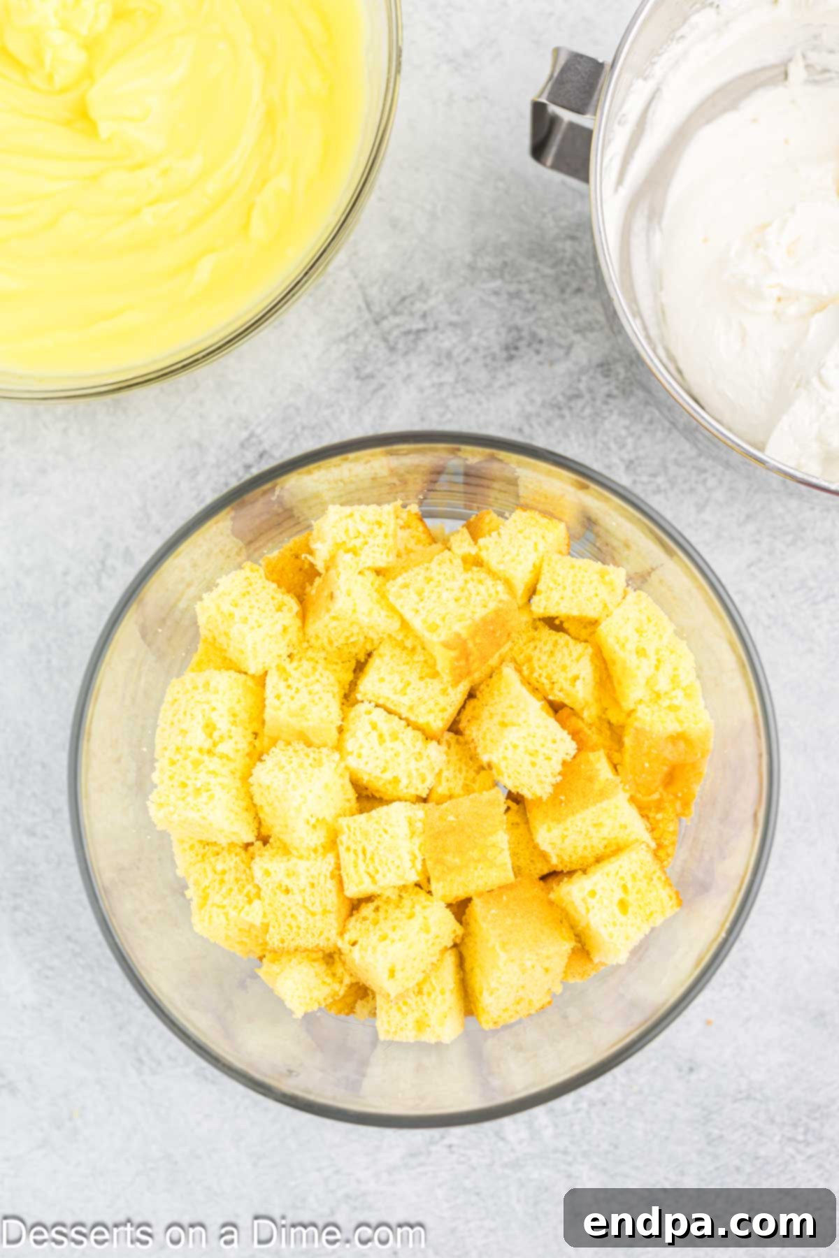 The first layer of cubed lemon cake placed at the bottom of a clear trifle dish.