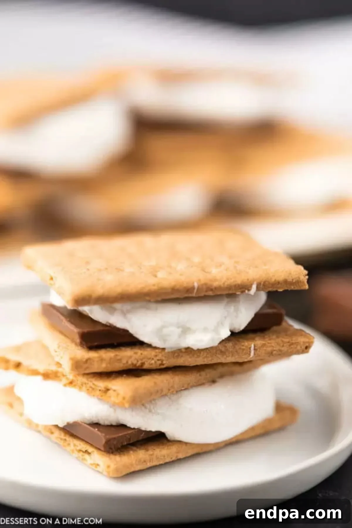 Oven baked smores are so convenient and you still can enjoy all the ooey gooey marshmallows and decadent chocolate. Try oven smores. Close-up of three stacked oven s'mores on a white plate