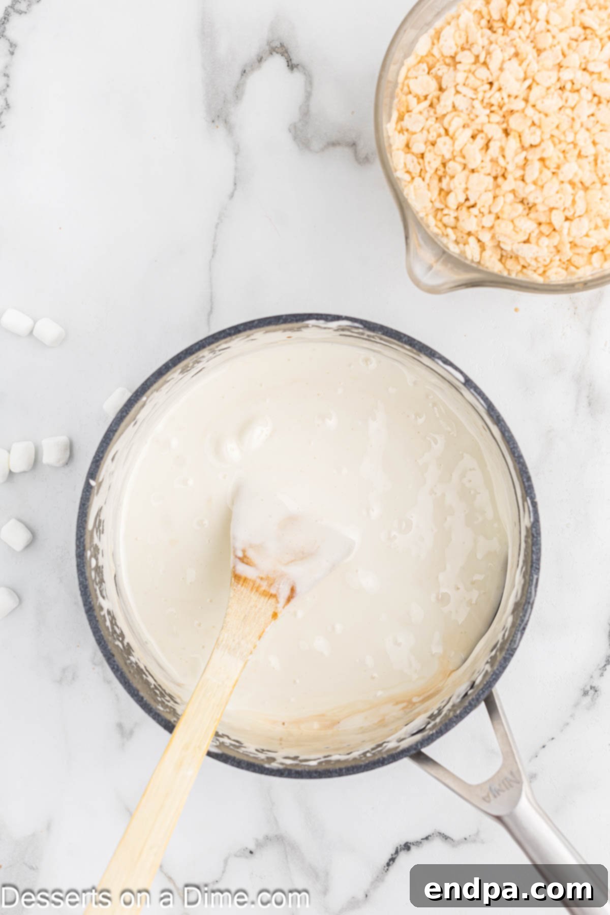 Mini marshmallows melting into the butter and corn syrup mixture in a saucepan.