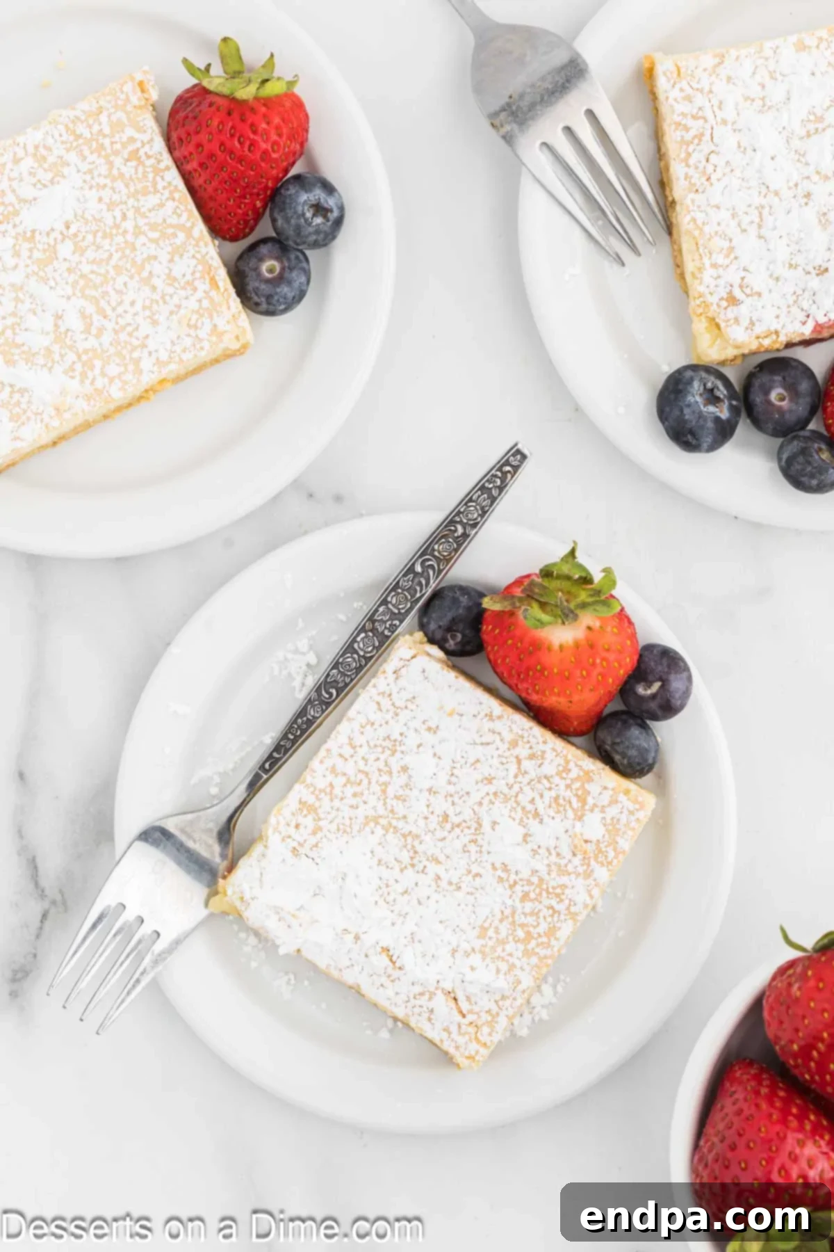 Paula Deen Ooey Gooey Butter Cake cut into squares and served on a plate with fresh berries and mint. 