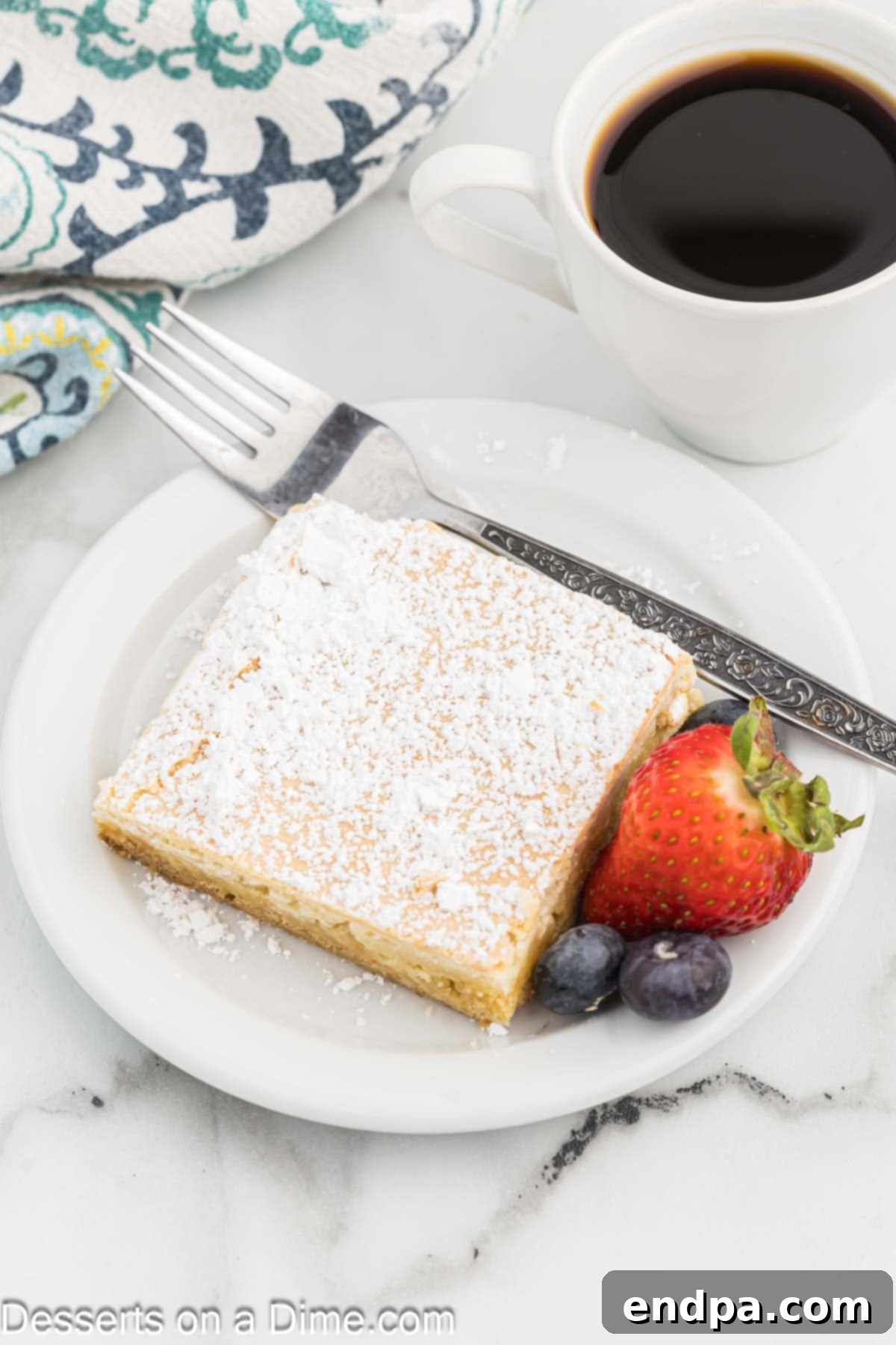 Paula Deen Ooey Gooey Butter Cake cut into squares and served on a plate with fresh strawberries and raspberries.