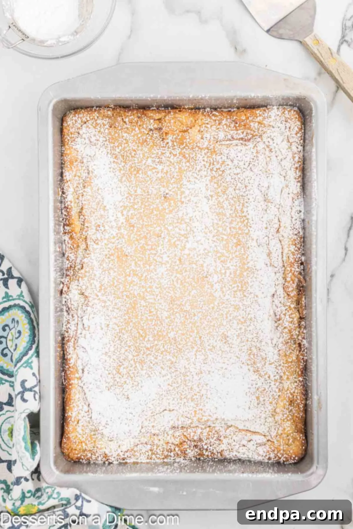 Powdered sugar being sprinkled generously over the cooled Ooey Gooey Butter Cake.