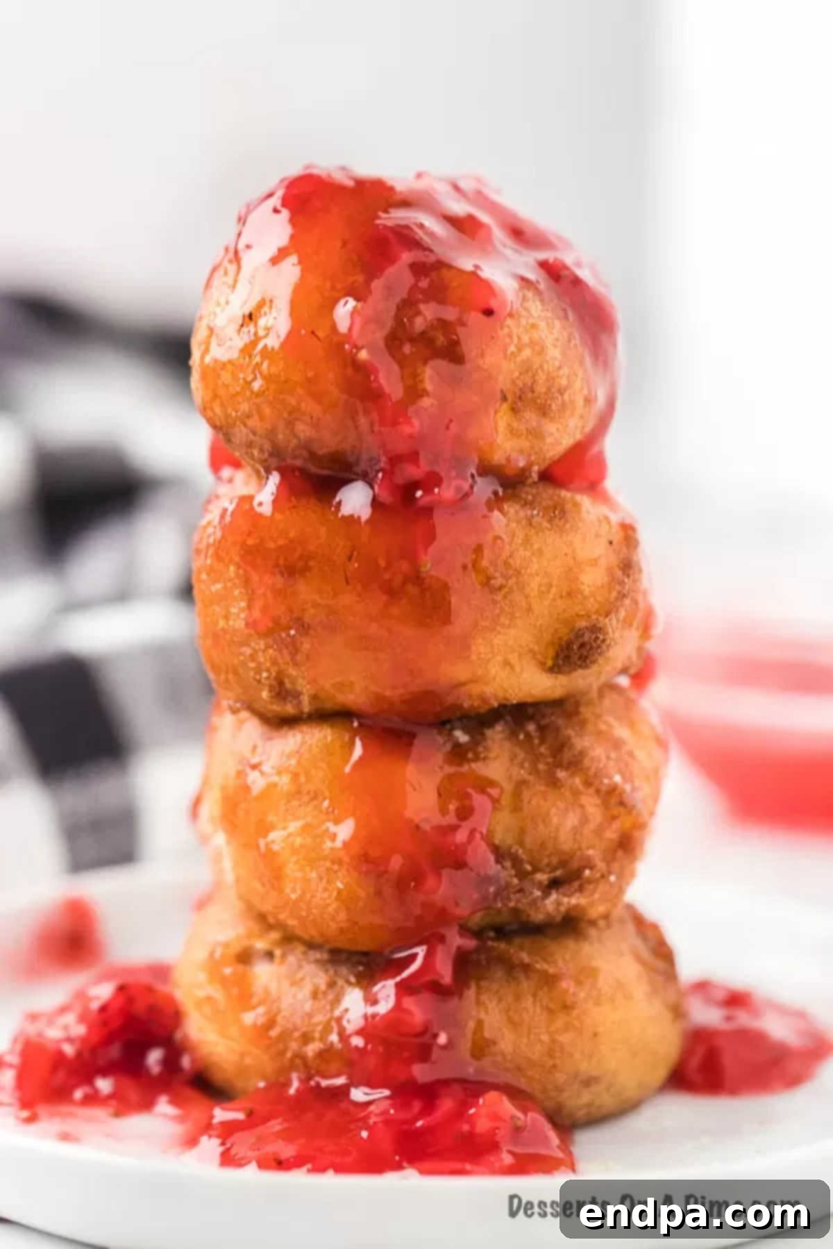 Crispy Cheesecake Indulgence 12 Close up image of Deep Fried Cheesecake Bites stacked and generously drizzled with fresh strawberry sauce.