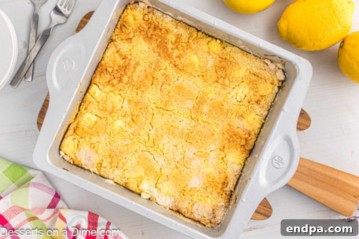 Zesty Lemon Easy Bake 2 A vibrant lemon dump cake served in a white baking dish, garnished with fresh lemon slices and a sprig of mint, set against a rustic wooden background with whole lemons scattered around.