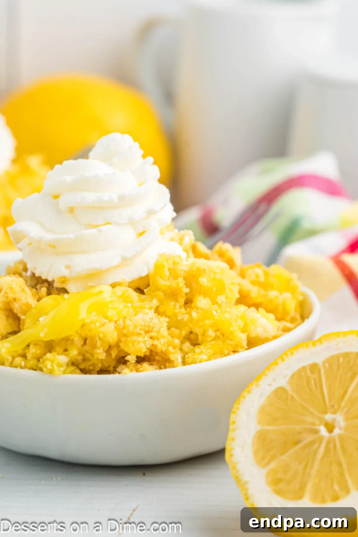 Zesty Lemon Easy Bake 11 A generous serving of lemon dump cake in a small white bowl, topped with a swirl of whipped cream and a sprinkle of lemon zest.