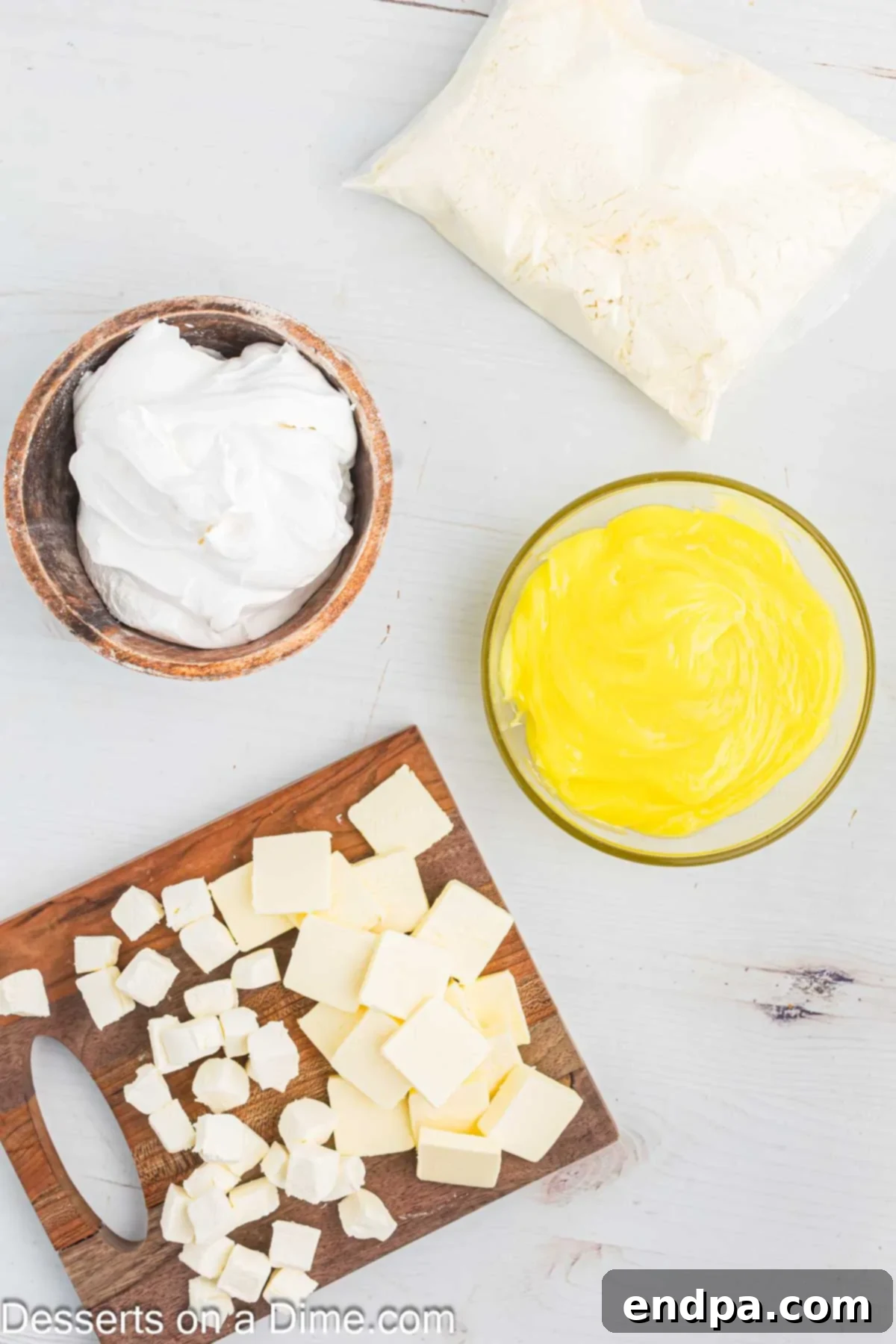 Zesty Lemon Easy Bake 4 Ingredients for Lemon Dump Cake including a yellow cake mix box, a block of cream cheese, a stick of butter, and a container of cool whip, arranged on a kitchen counter.
