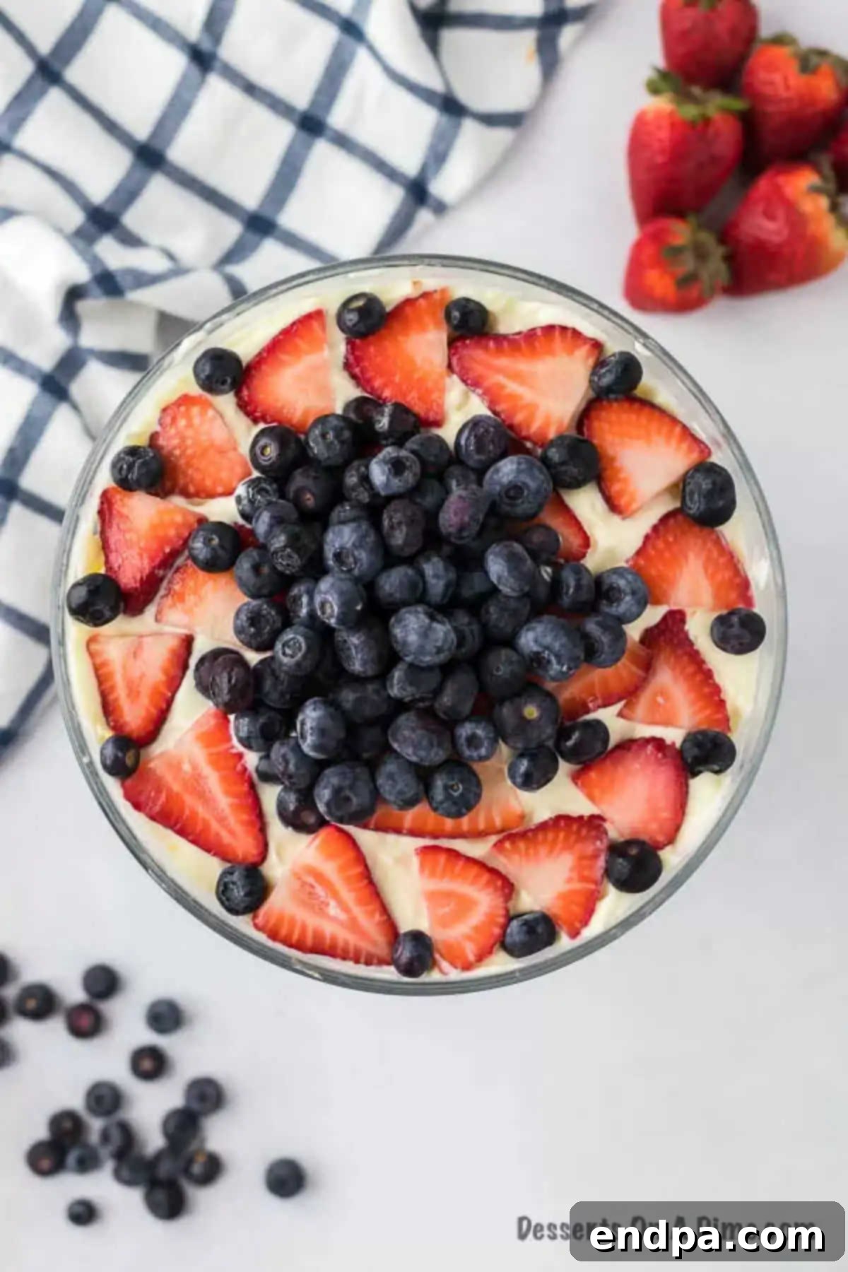 A stunning Red White and Blue Trifle in a clear glass container, adorned with fresh strawberries and blueberries on top.