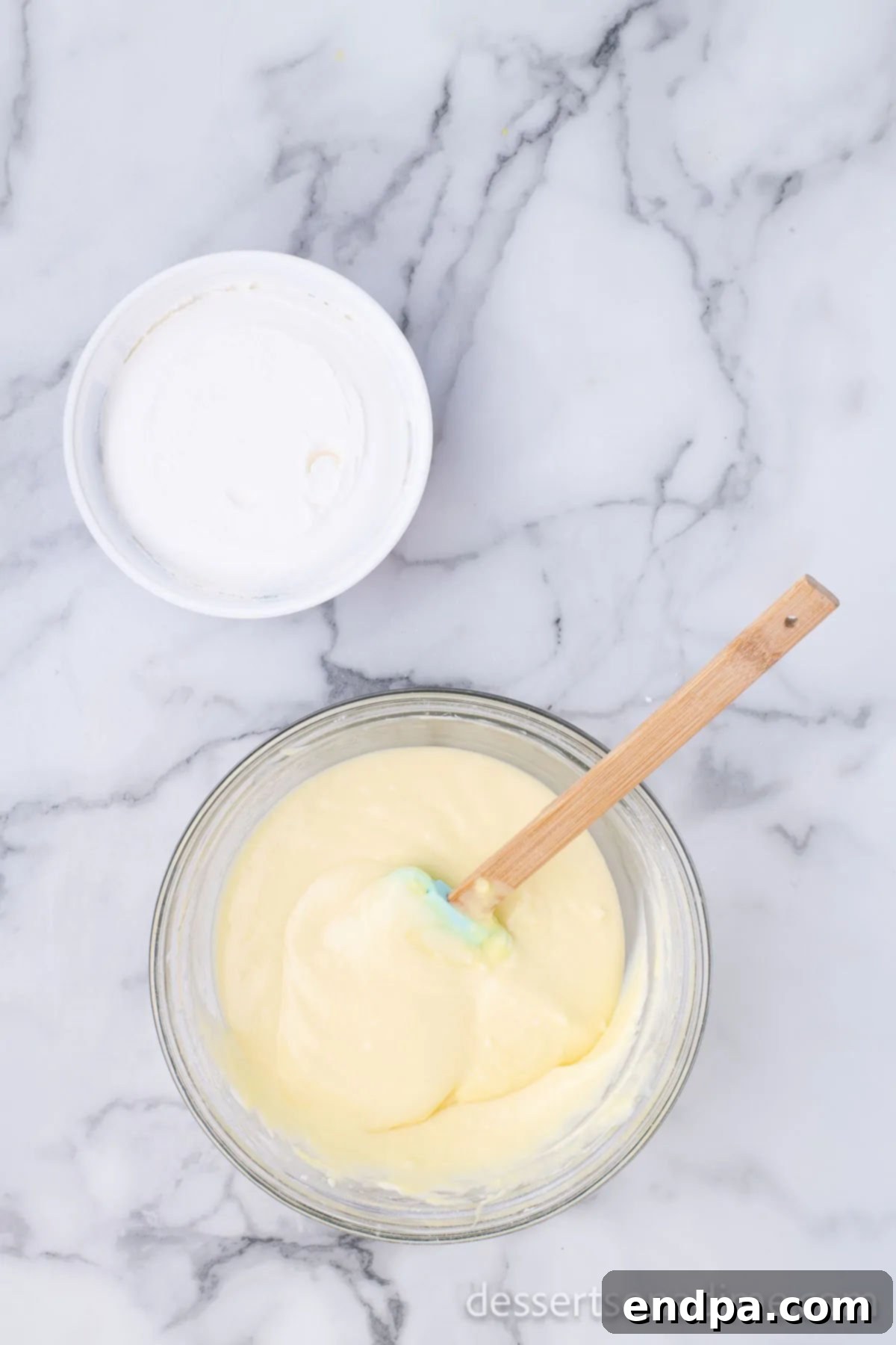 Cool Whip being gently folded into the pudding and cream cheese mixture in a bowl.