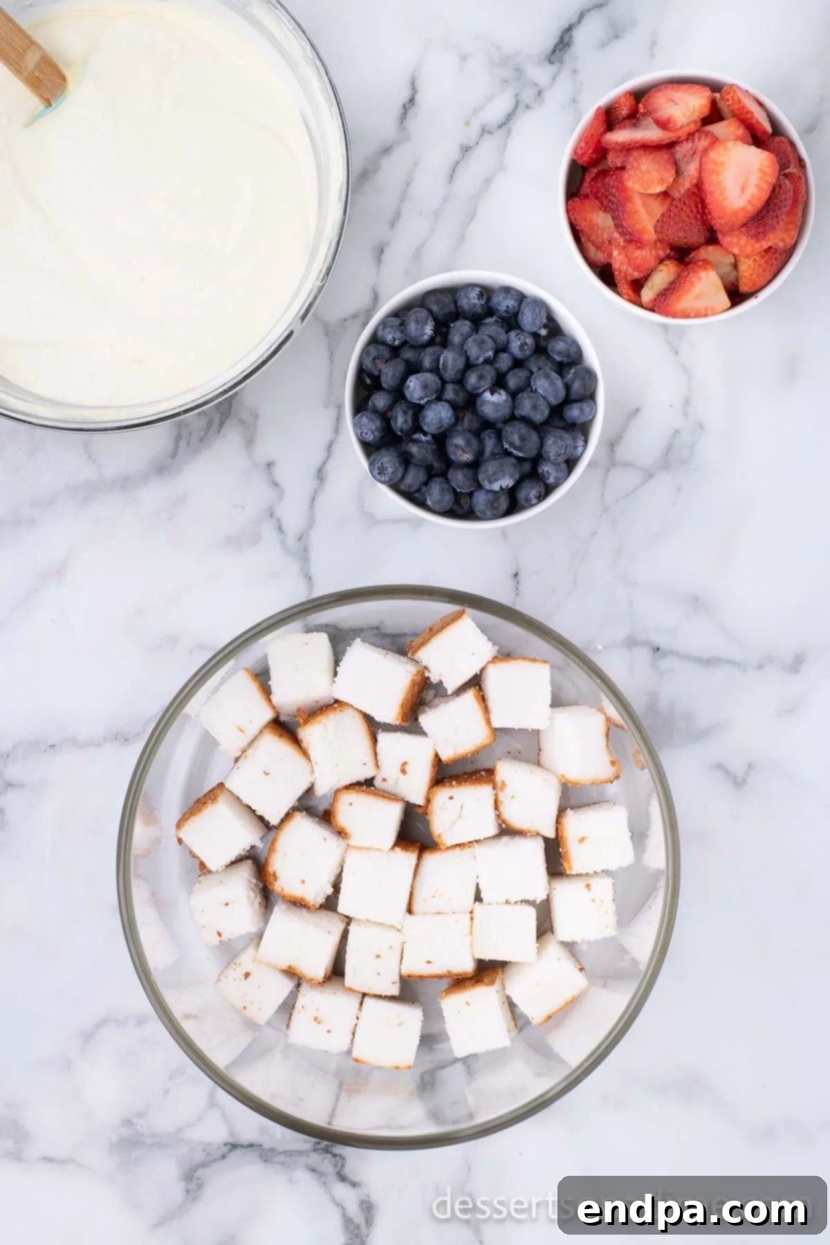 A layer of cubed angel food cake neatly arranged at the bottom of a glass trifle dish.