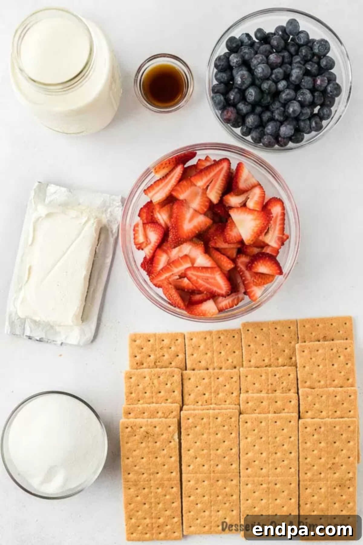 Ingredients for Red White and Blue Icebox Cake: fresh strawberries, blueberries, graham crackers, a block of cream cheese, a carton of heavy whipping cream, and a bottle of vanilla extract are arranged on a white surface.