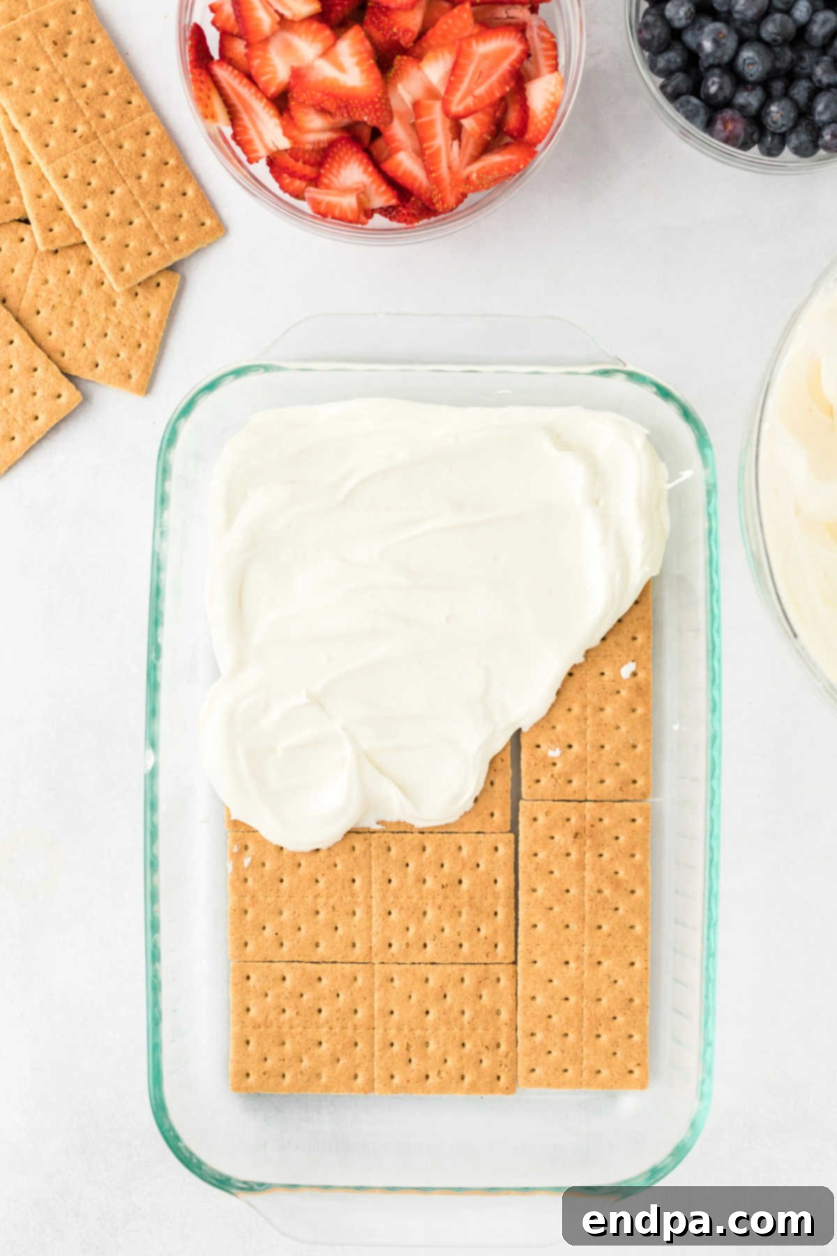 A smooth layer of the cream cheese mixture is spread evenly over the graham crackers in a baking dish.