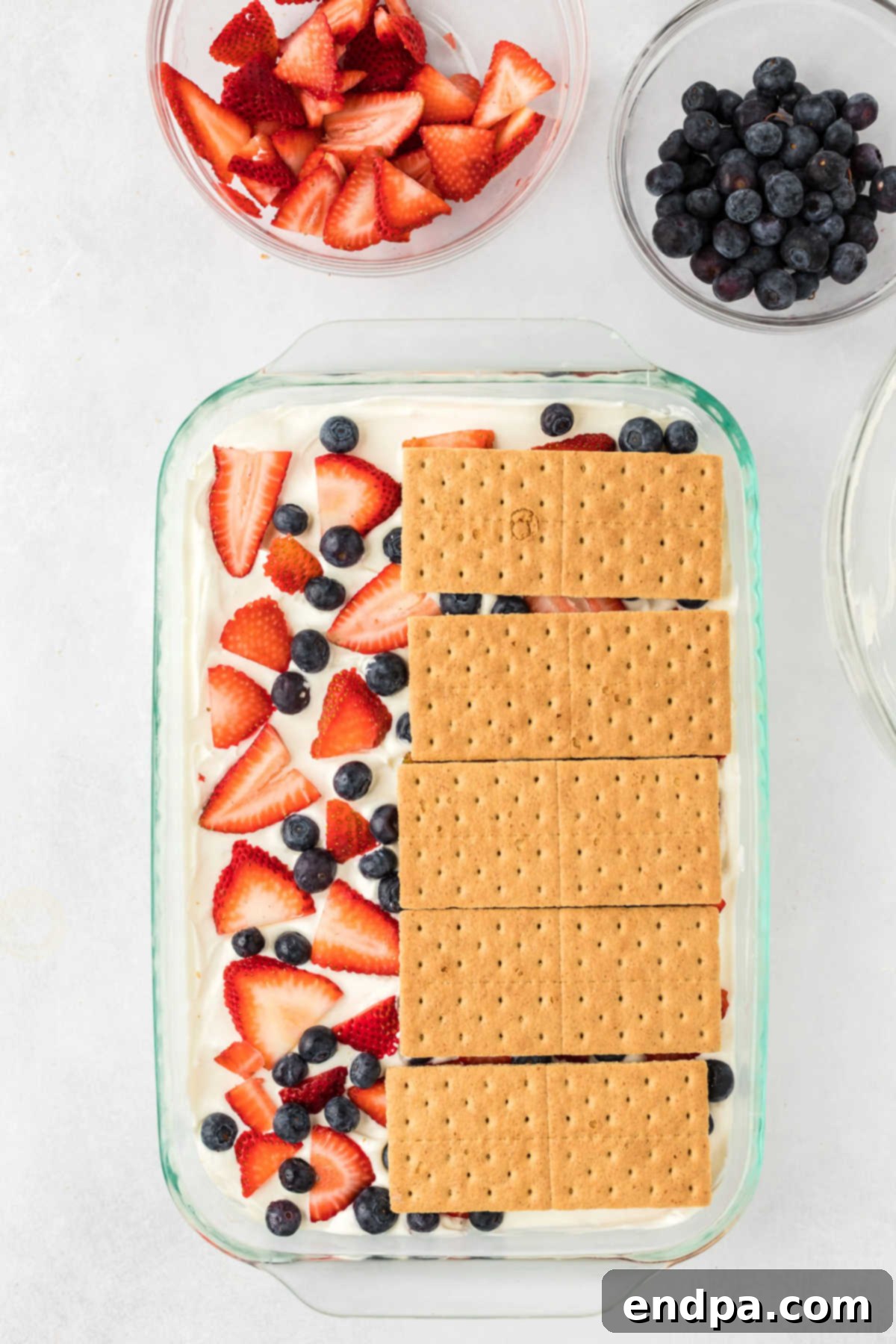 Another layer of graham crackers is placed on top of the berry and cream layer, continuing the icebox cake construction.