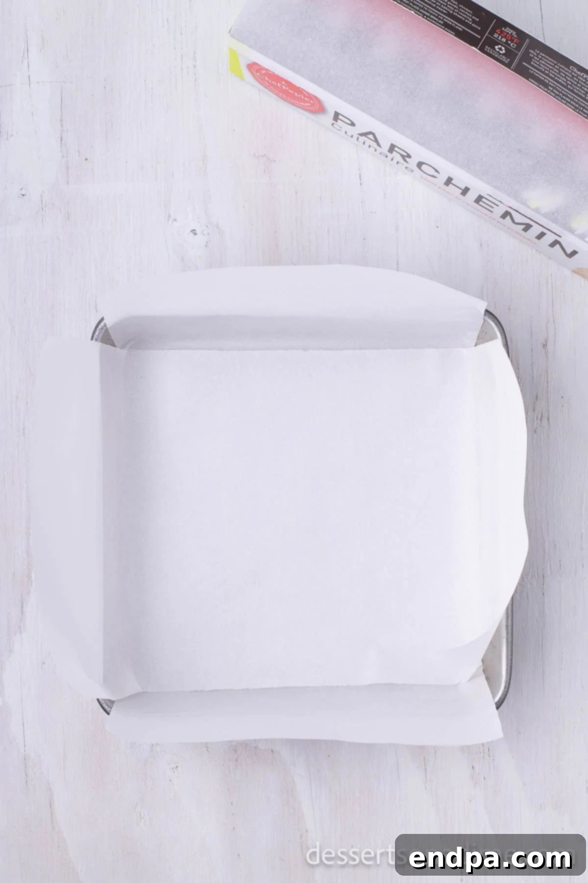 A 9x9 inch baking pan meticulously lined with parchment paper, ensuring easy removal of the chocolate fudge.