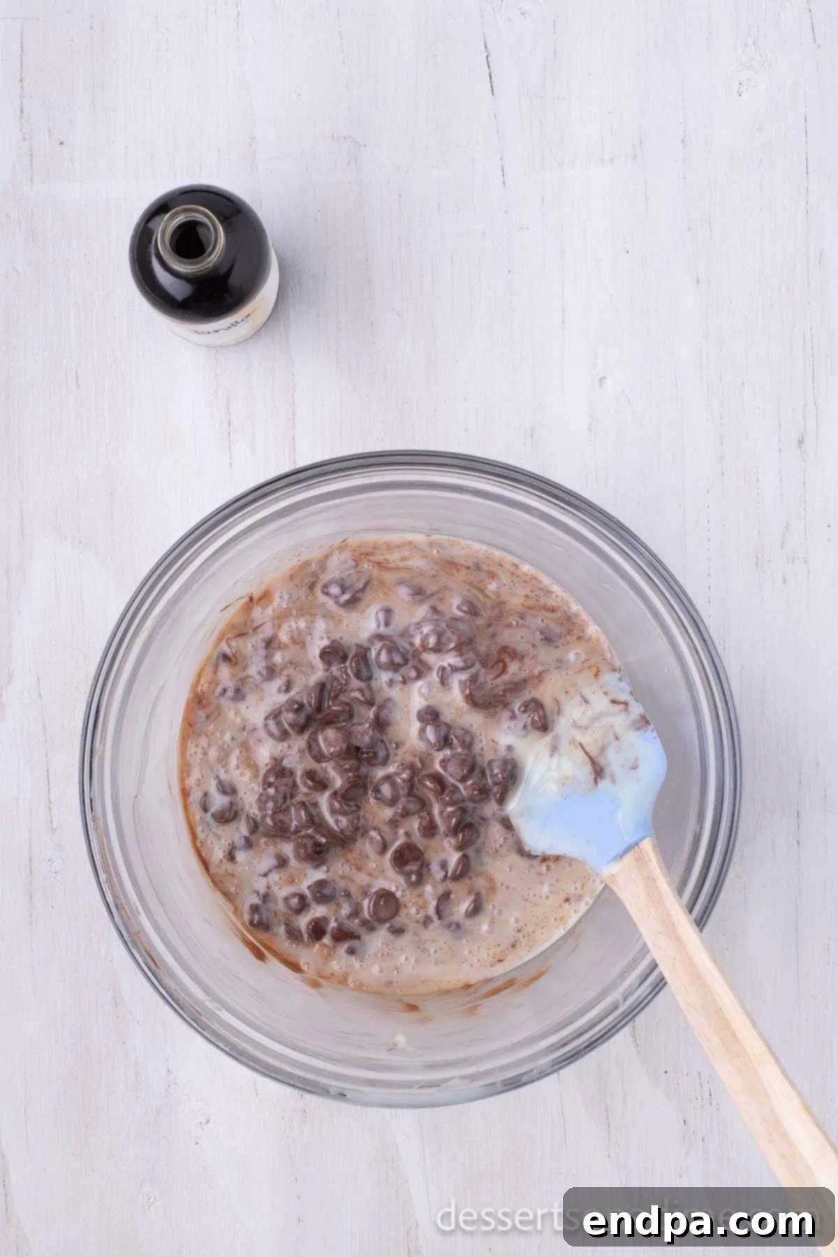 A wooden spoon stirring together the luscious mixture of melted chocolate chips and sweetened condensed milk in a bowl.
