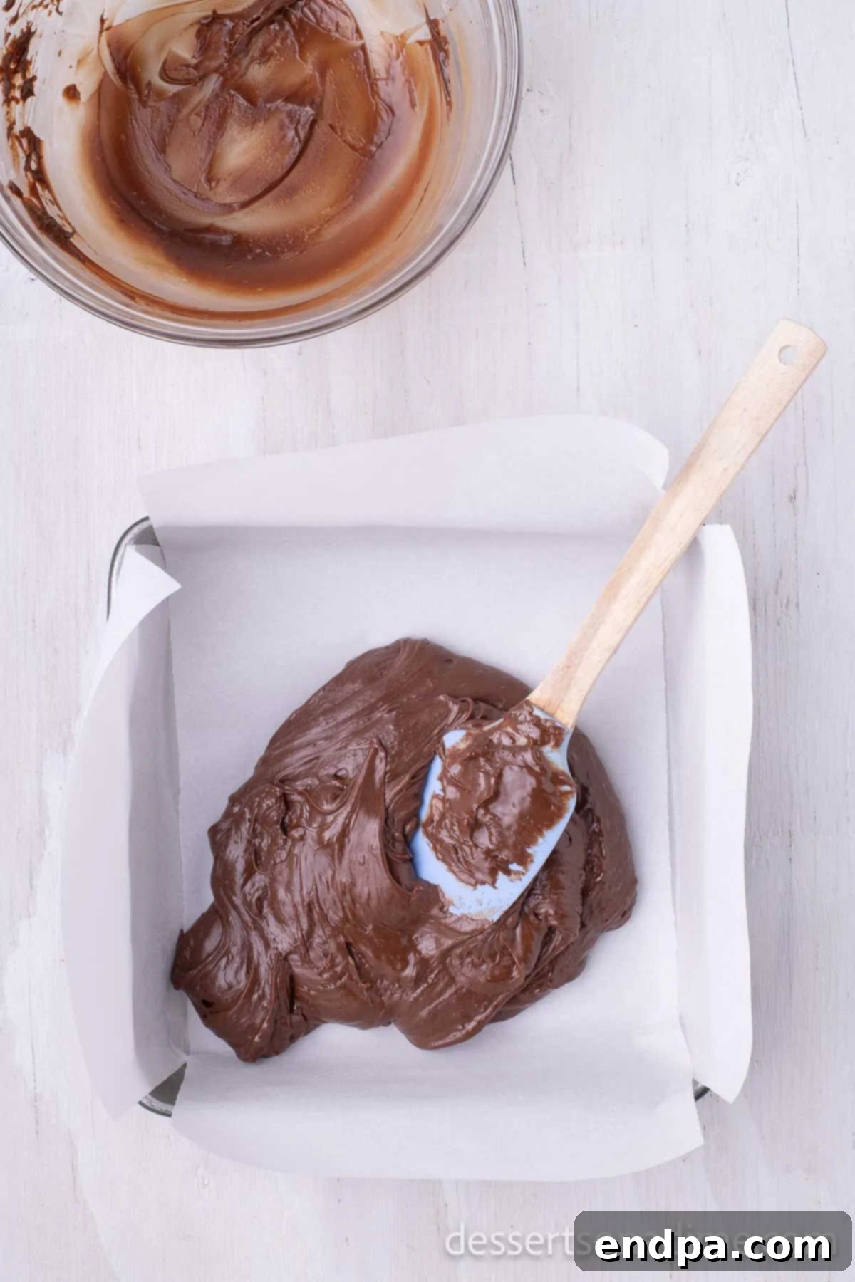 The warm, rich chocolate fudge mixture being quickly and smoothly spread into the prepared pan.