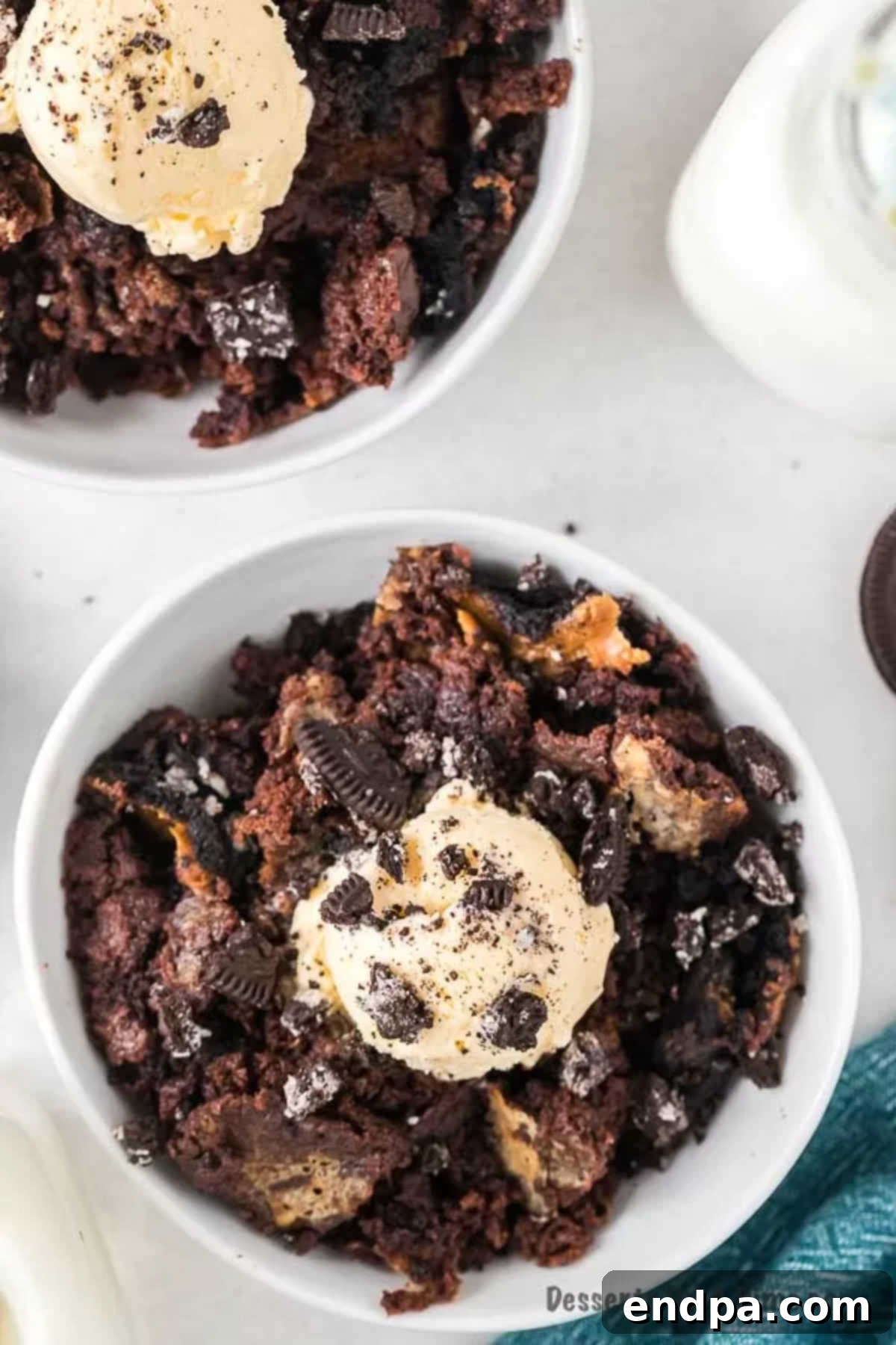 Irresistible Oreo Dump Cake 2 The top view of a rich, chocolatey Oreo Dump Cake, generously topped with a scoop of creamy vanilla ice cream and delicate crushed Oreos, artfully presented in a pristine white bowl.