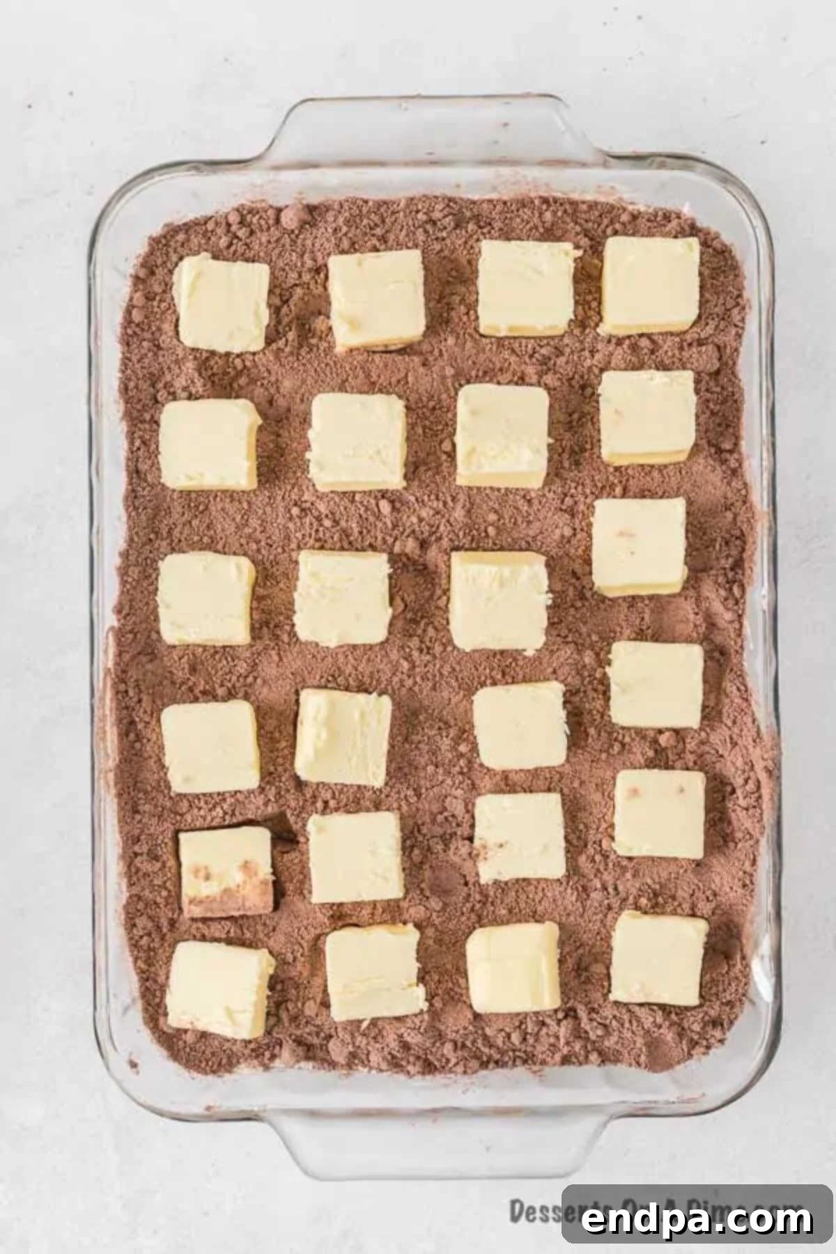 Irresistible Oreo Dump Cake 9 Thin, cold slices of butter meticulously placed on top of the dry cake mix layer in the baking pan, ensuring even coverage before baking to create a moist and flavorful cake.