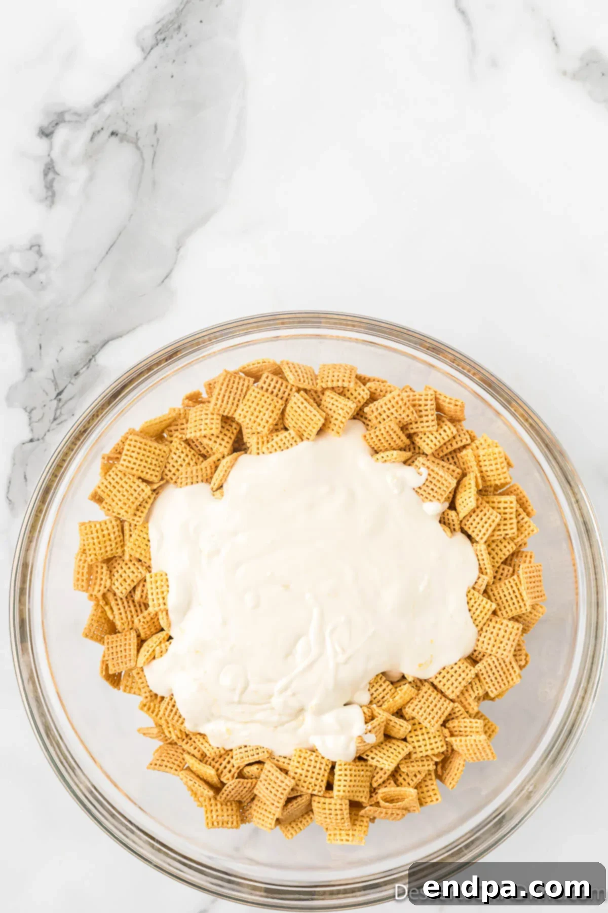 Melted lemon white chocolate being poured over Chex cereal in a large bowl.