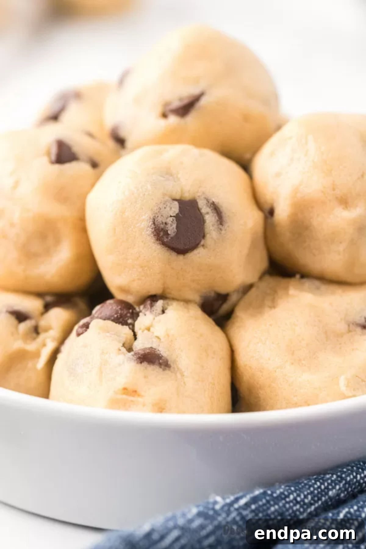 Ready-to-Eat Cookie Dough Dream 8 A stack of freshly made edible cookie dough balls, showcasing their perfectly round shape and tempting chocolate chips, on a rustic platter.