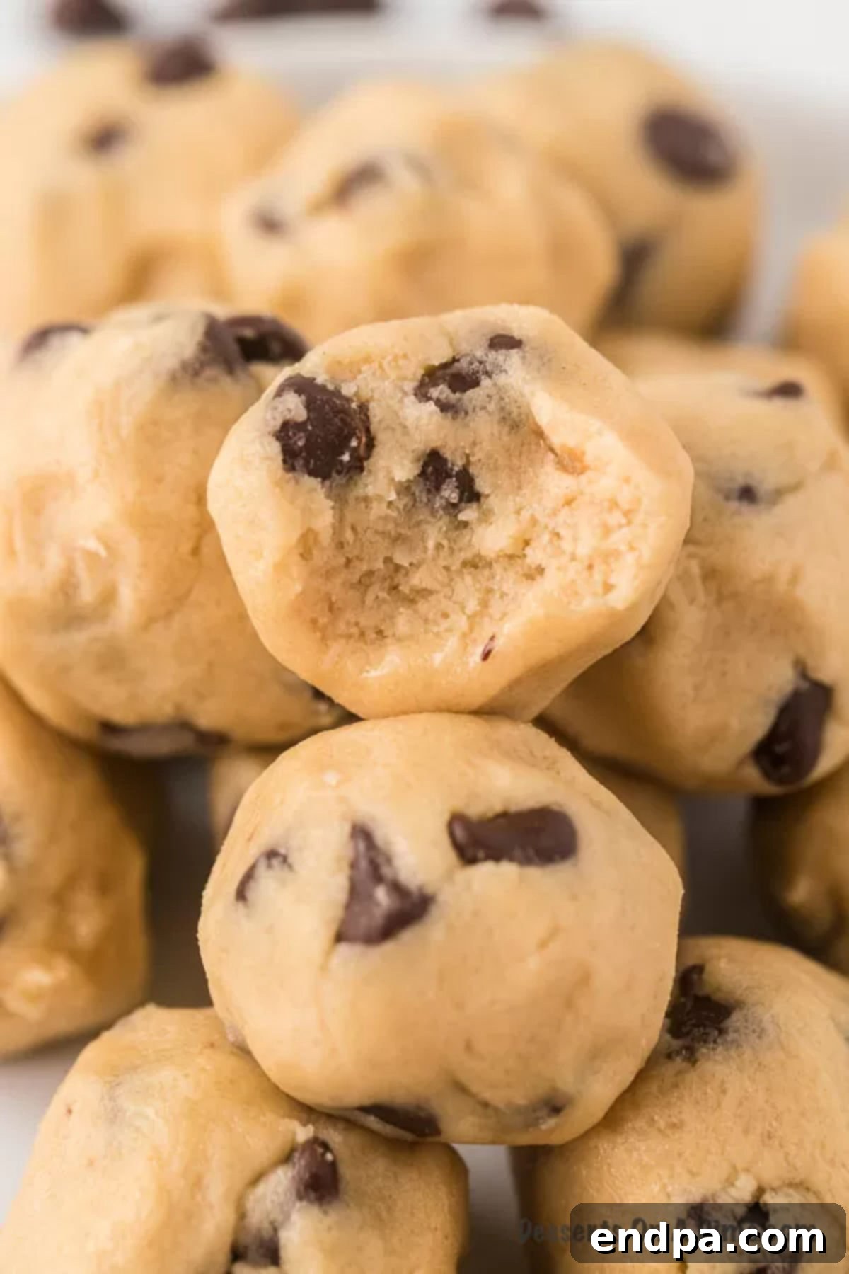 Ready-to-Eat Cookie Dough Dream 9 Close-up view of two stacks of edible cookie dough balls, garnished with extra chocolate chips, on a white plate.