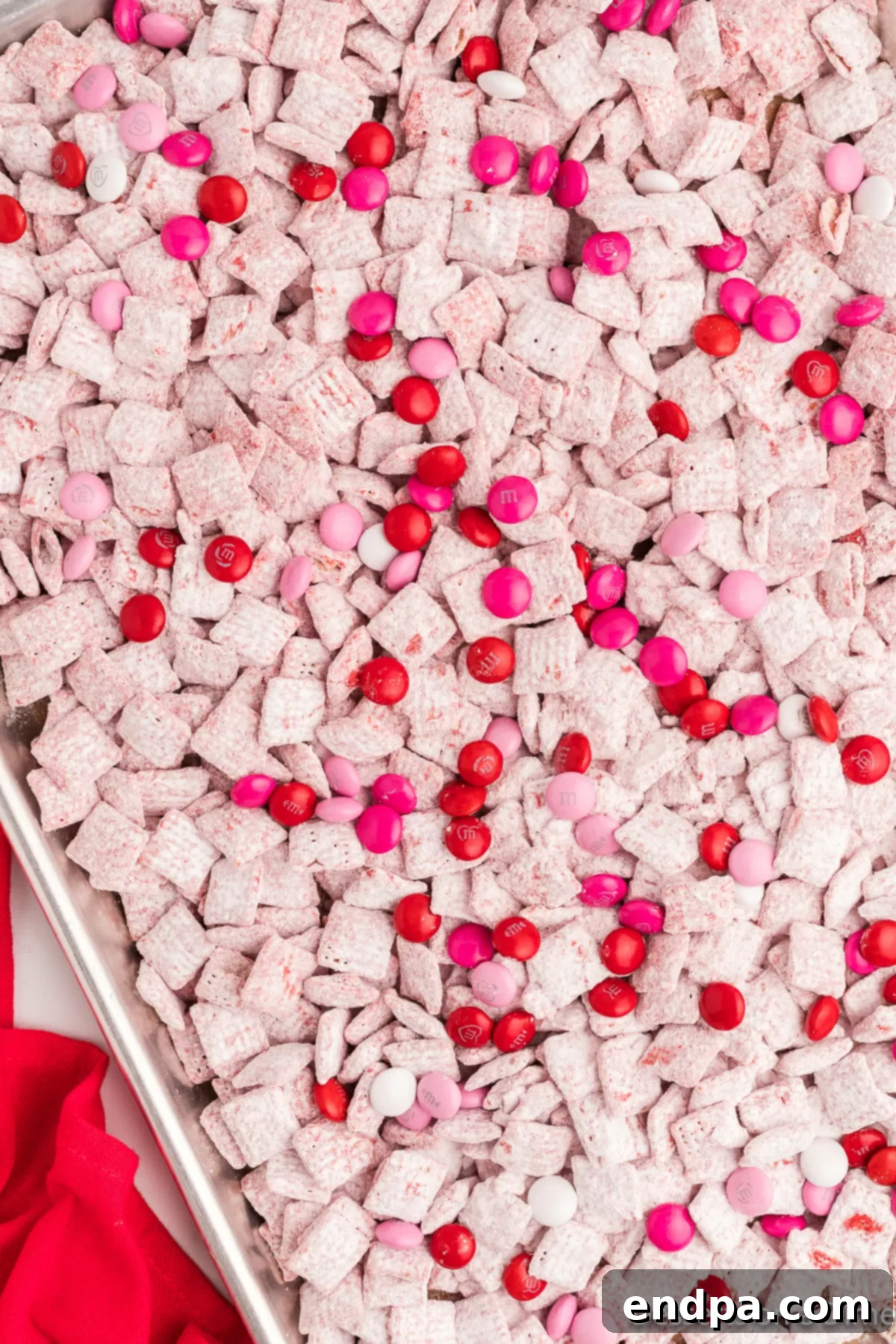 Valentine's M&Ms and sprinkles being added to the powdered sugar-coated puppy chow mixture.