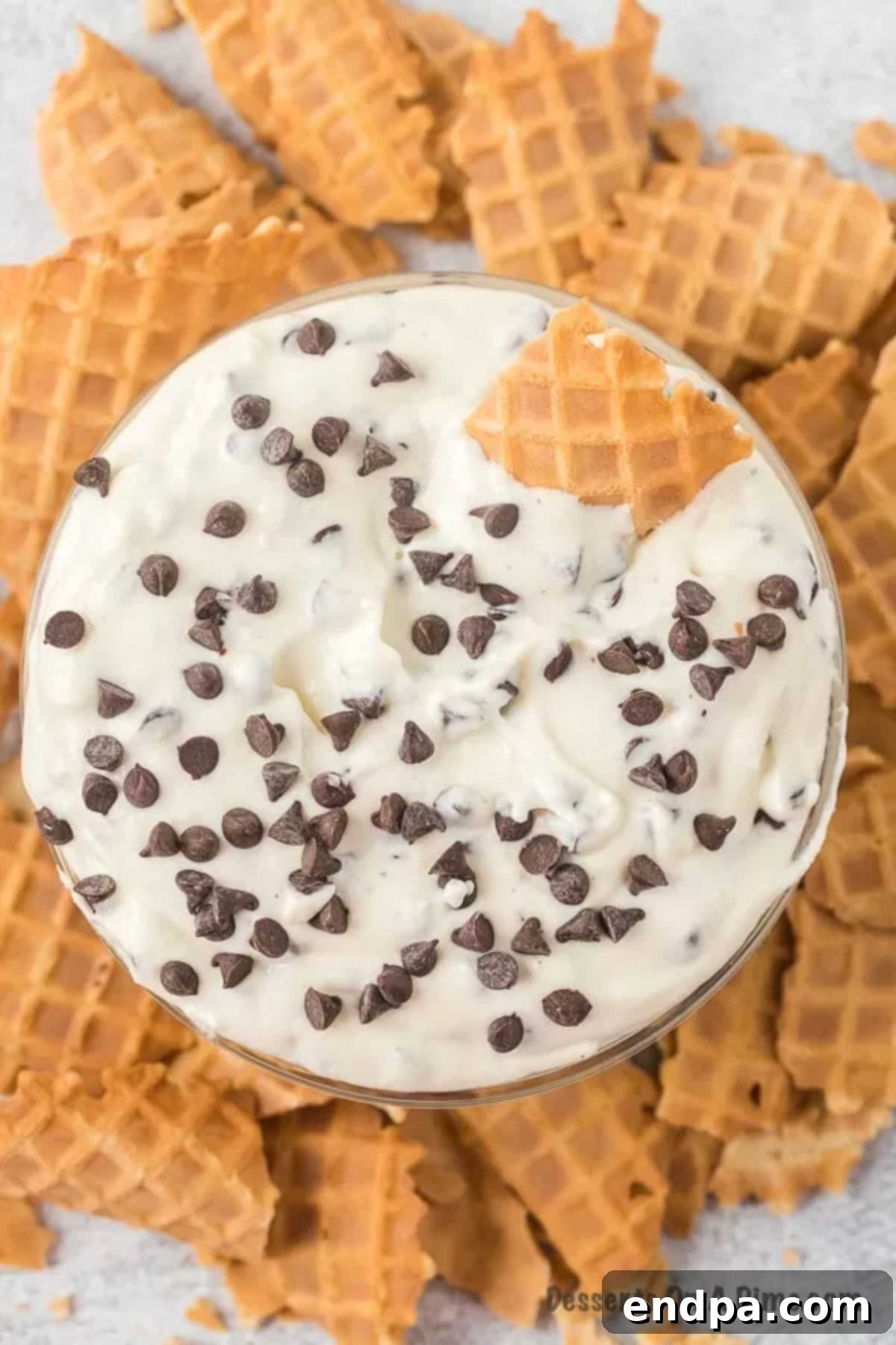 Creamy cannoli dip in a decorative bowl, surrounded by crispy waffle cone pieces and a sprinkle of mini chocolate chips, ready for dipping.