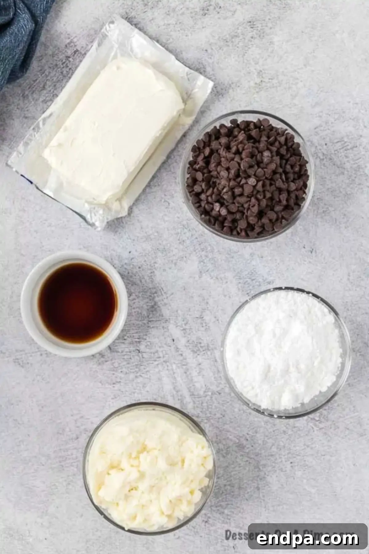 The five key ingredients for cannoli dip: cream cheese, ricotta cheese, powdered sugar, vanilla extract, and mini chocolate chips, laid out on a clean surface.