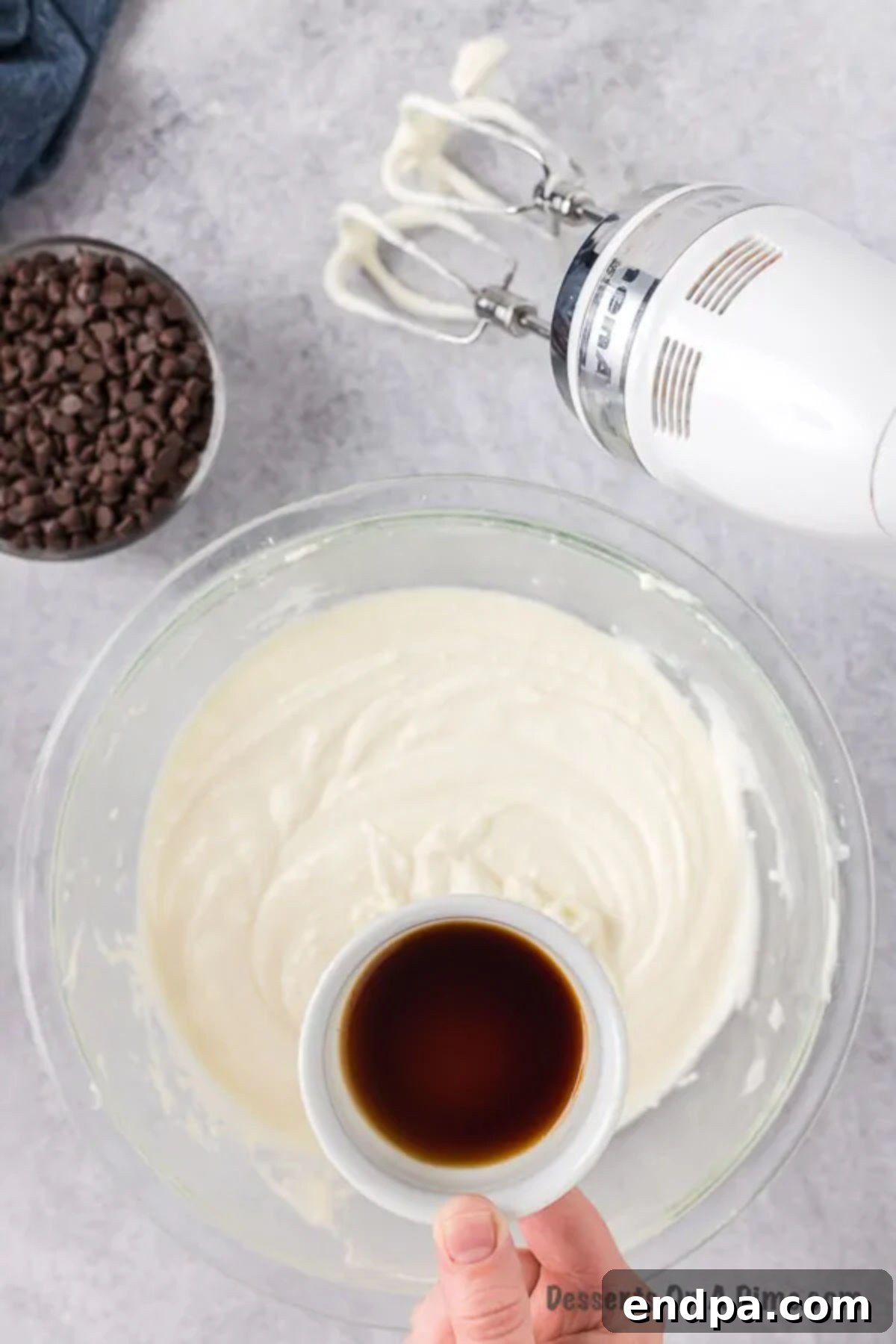 Vanilla extract being poured into the whipped cream cheese and ricotta mixture in a bowl, ready to be combined.