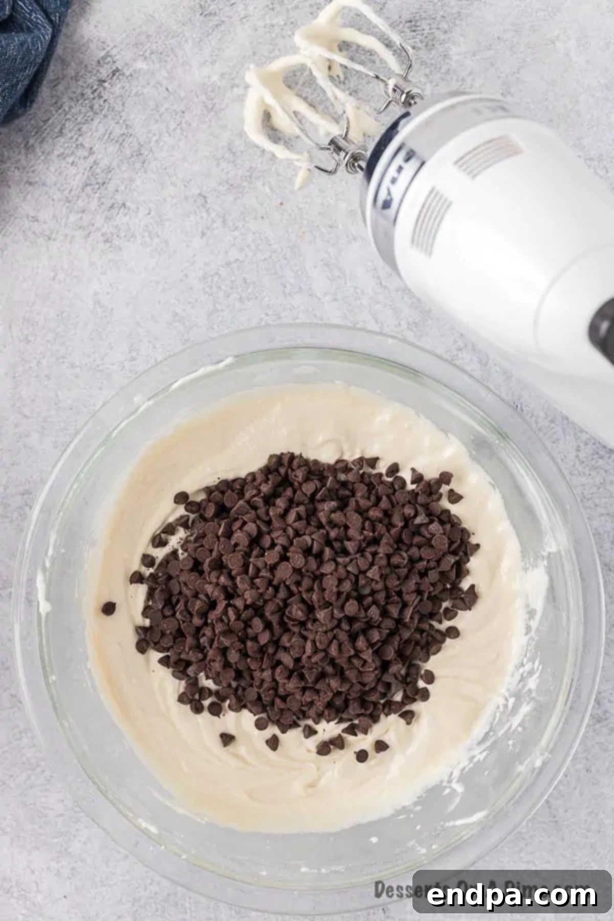 Miniature chocolate chips being gently folded into the prepared cannoli dip mixture with a spatula, ensuring even distribution.