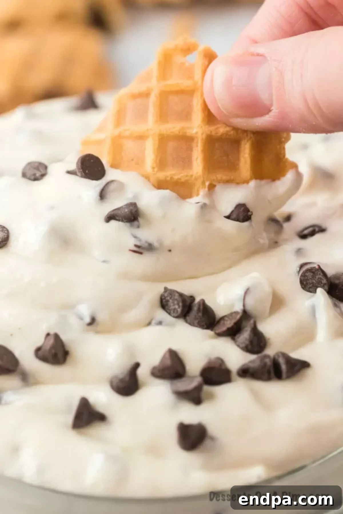 A person dipping a crispy waffle cone piece into a bowl of creamy cannoli dip, showcasing its perfect consistency.
