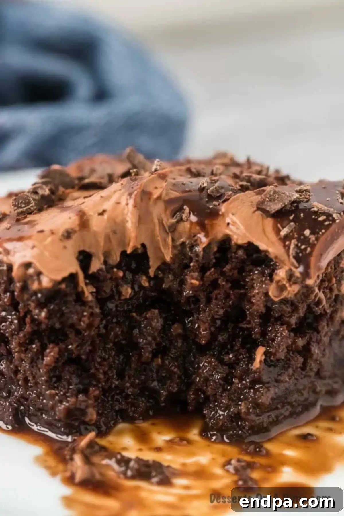 A delectable slice of chocolate poke cake on a pristine white plate, showcasing its rich layers and tempting chocolate drizzle.