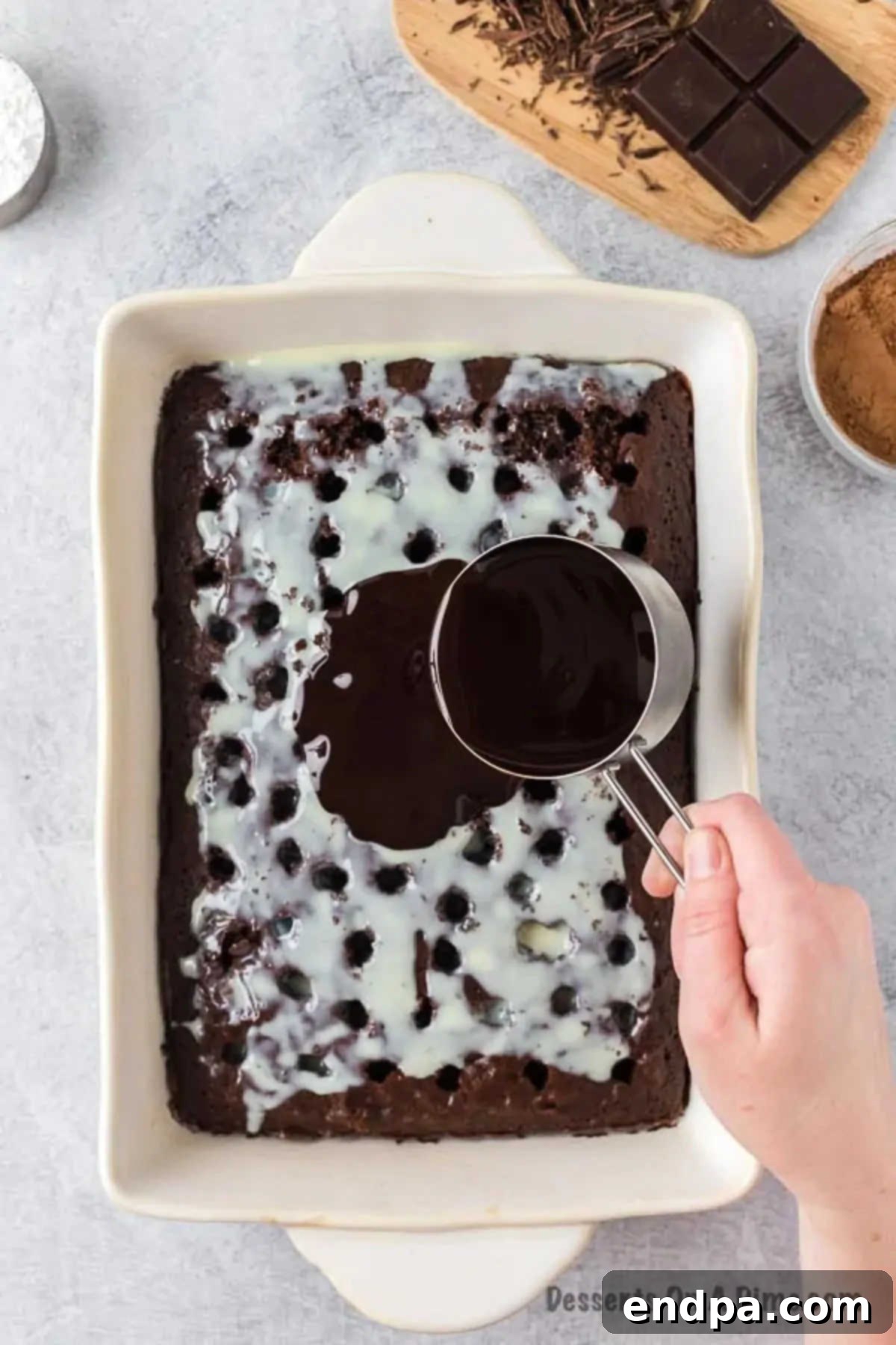 Sweetened condensed milk and rich chocolate sauce being generously poured over the poked holes of the chocolate cake.