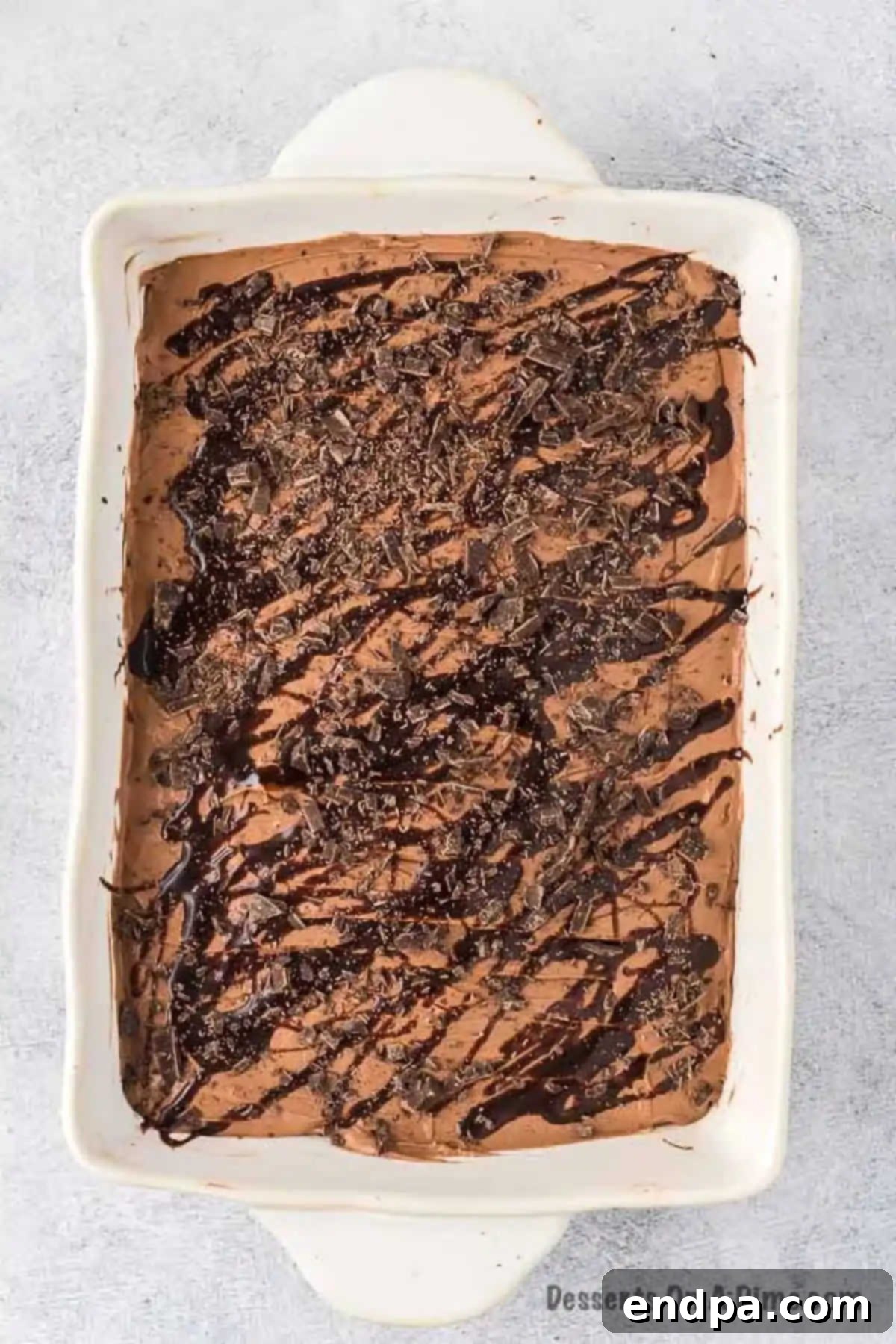 The finished chocolate poke cake, generously topped with chocolate whipped cream and a final drizzle of chocolate sauce and chopped chocolate.