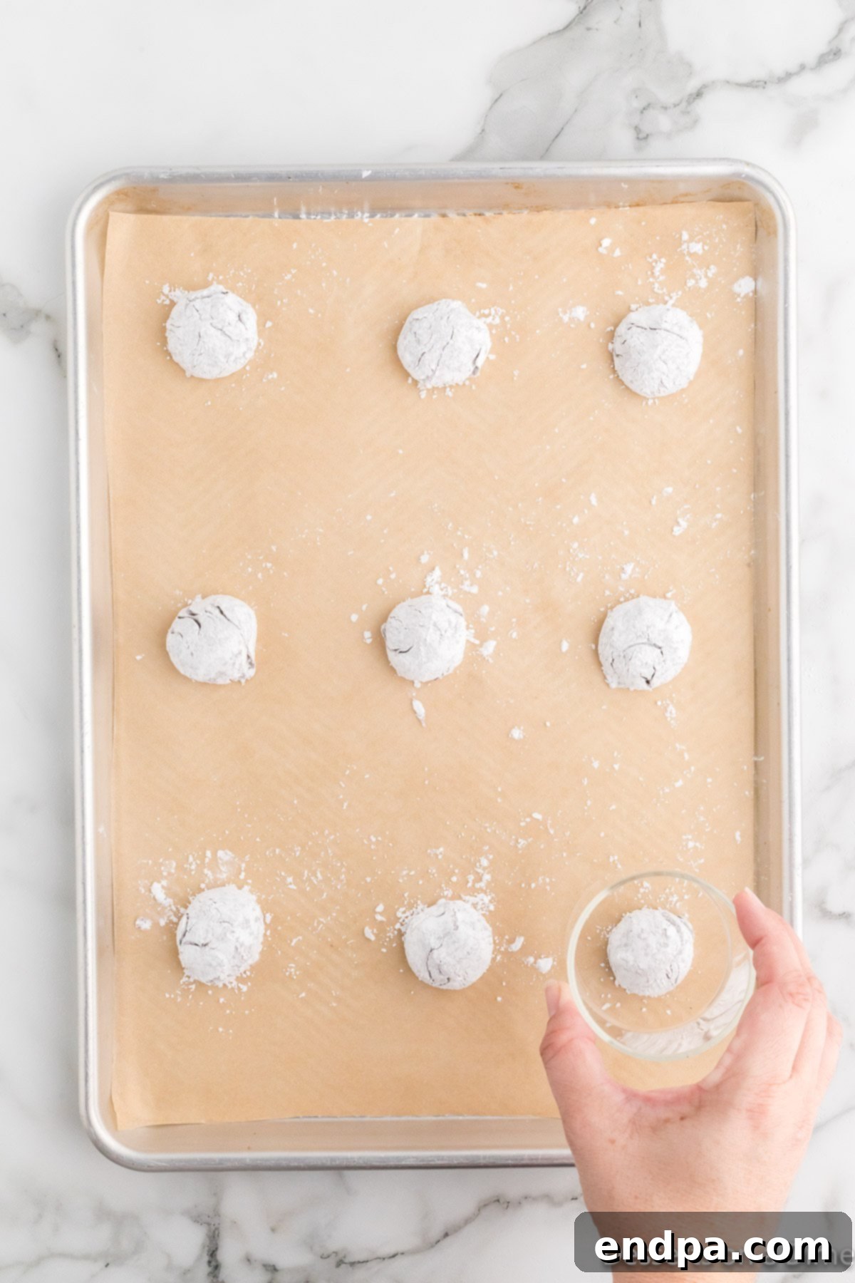Cracked Cocoa Bliss 8 A glass gently pressing down on a cookie dough ball on a baking sheet.
