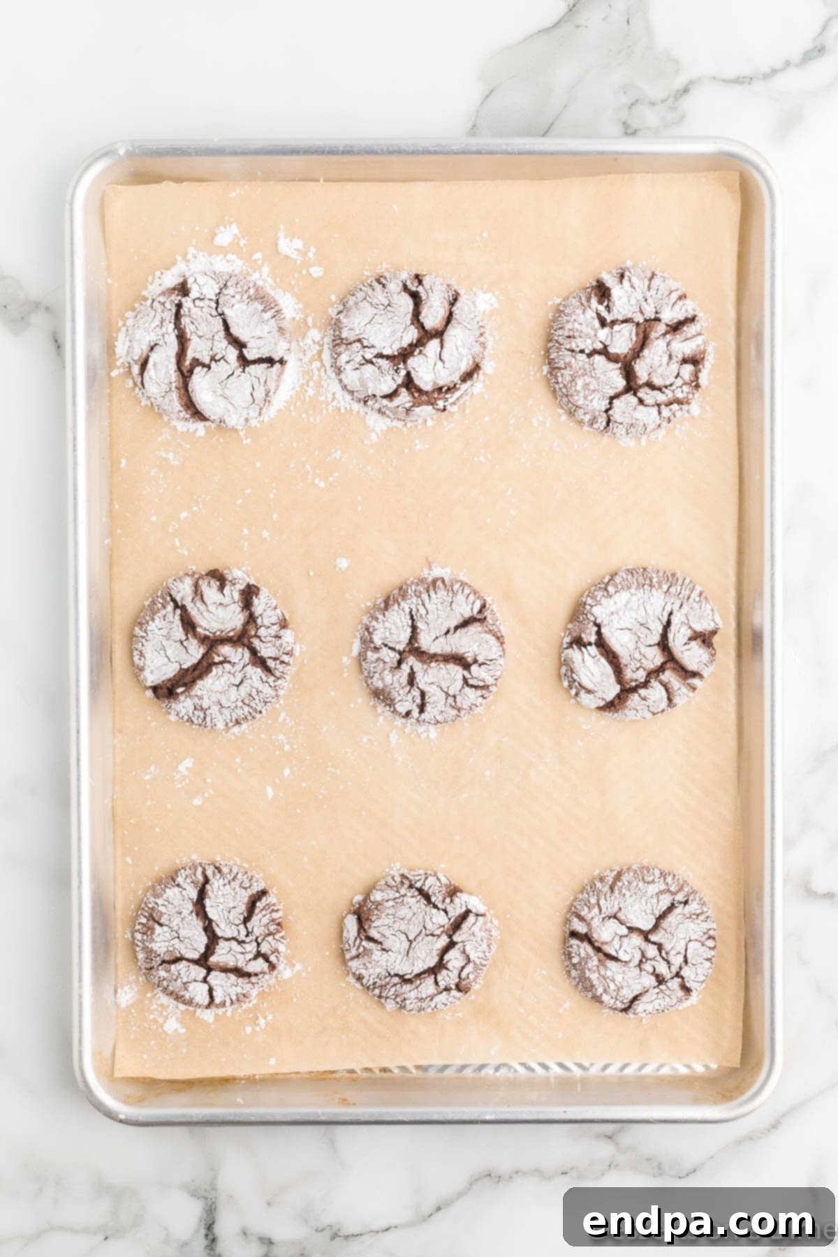 Cracked Cocoa Bliss 9 Baked chocolate crinkle cookies cooling on a baking sheet.