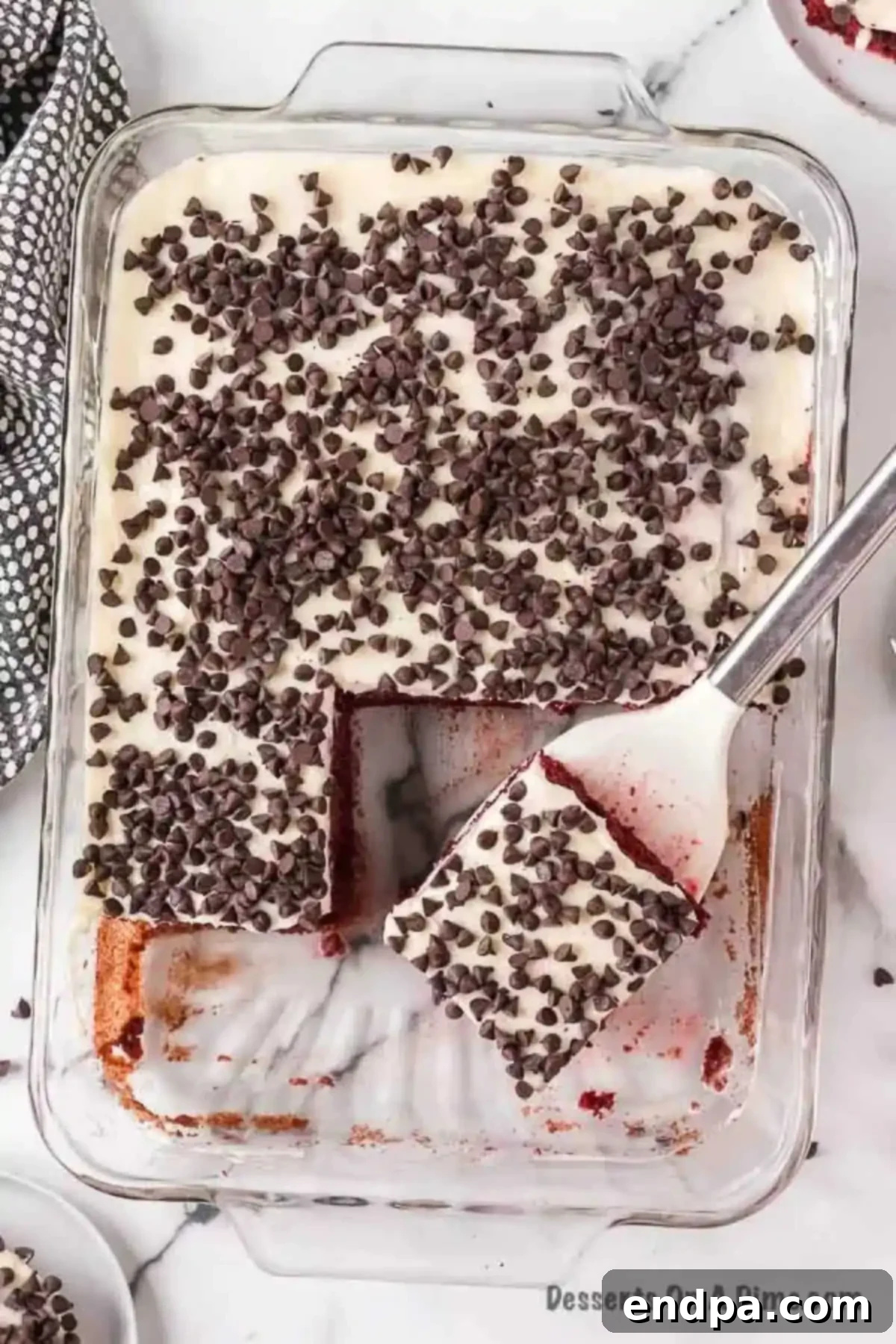 Red Velvet Infusion Cake 11 Red Velvet Poke Cake in a baking dish with a spatula ready for serving.