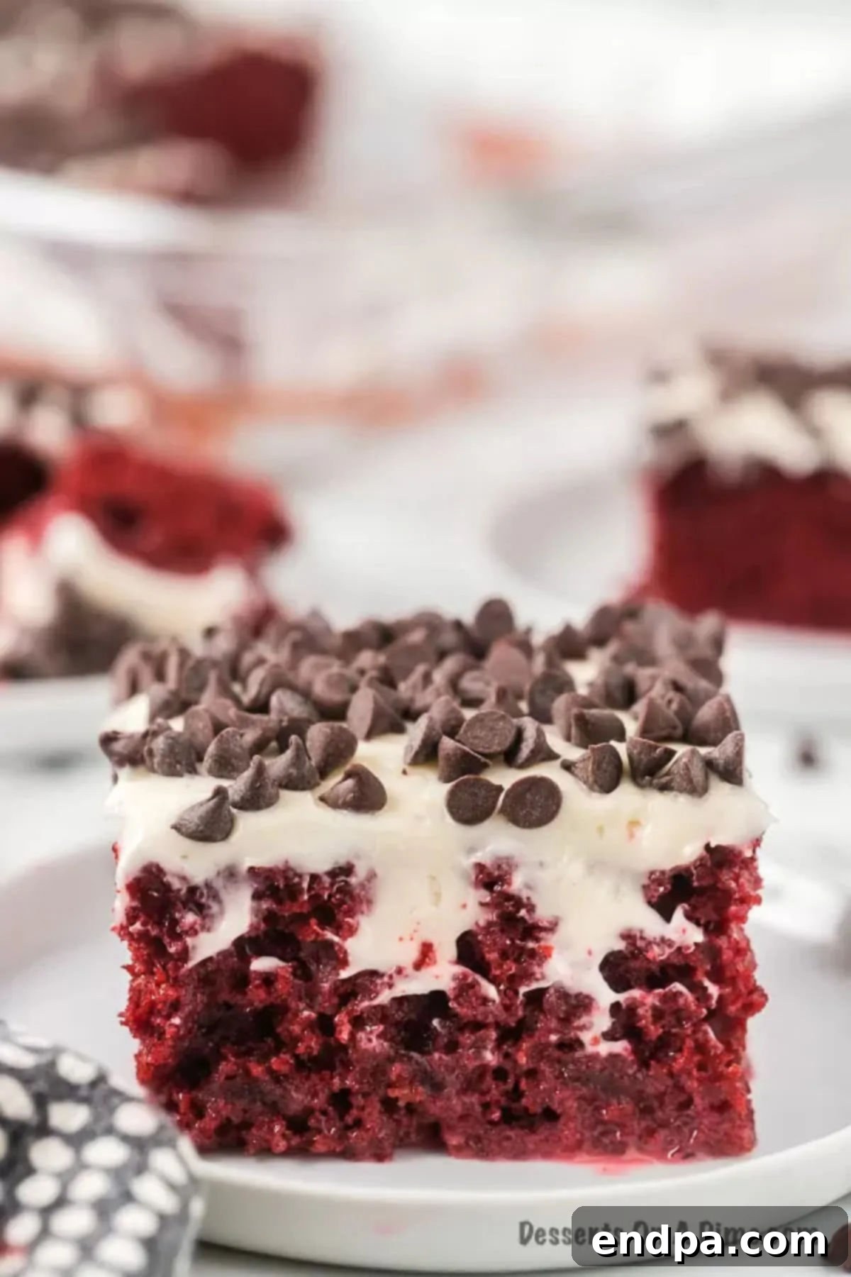 Red Velvet Infusion Cake 4 A perfectly sliced piece of Red Velvet Poke Cake on a plate, revealing its moist, red layers and creamy white frosting.