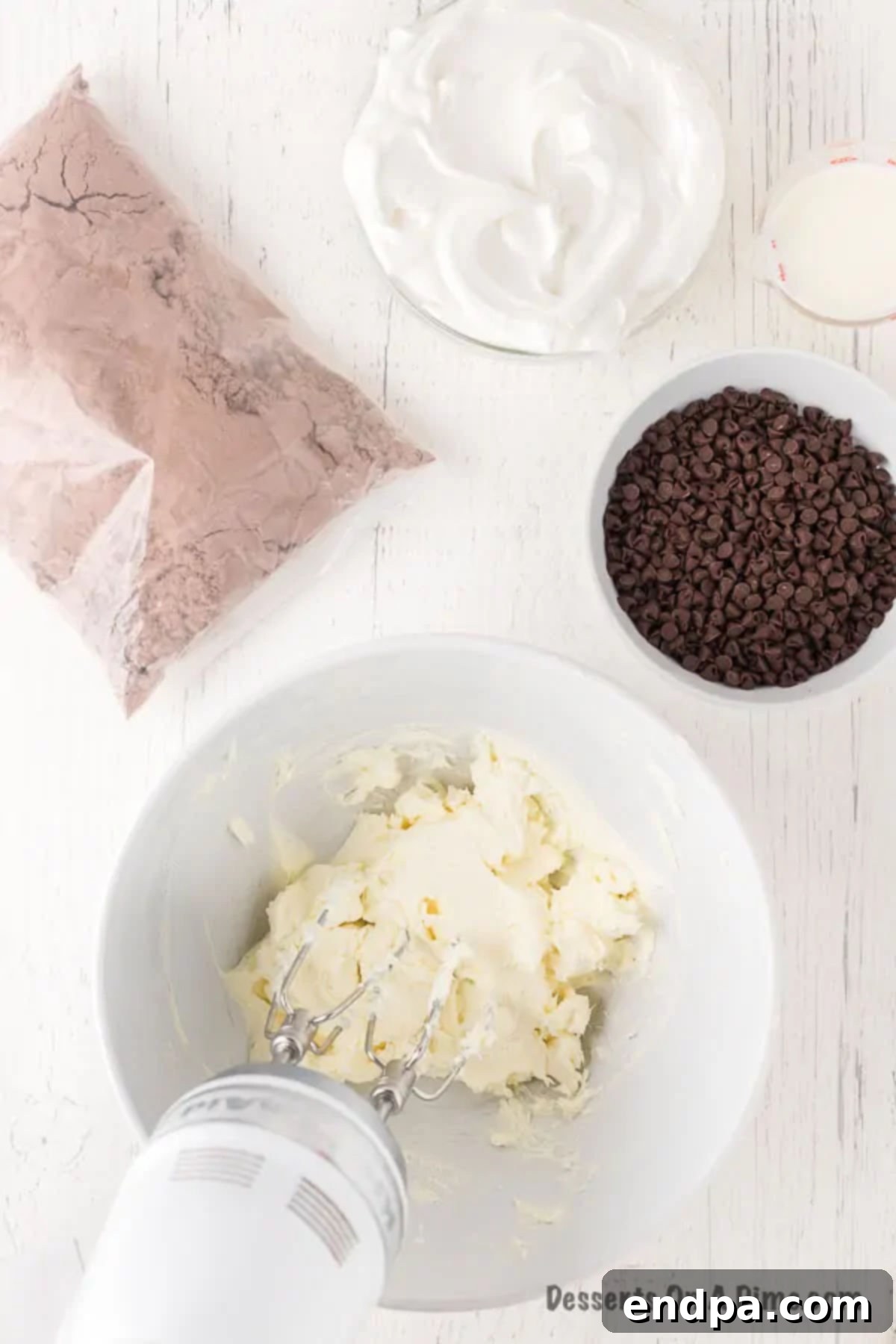 Decadent Brownie Dip 4 Softened cream cheese being beaten in a bowl with a hand mixer until smooth.