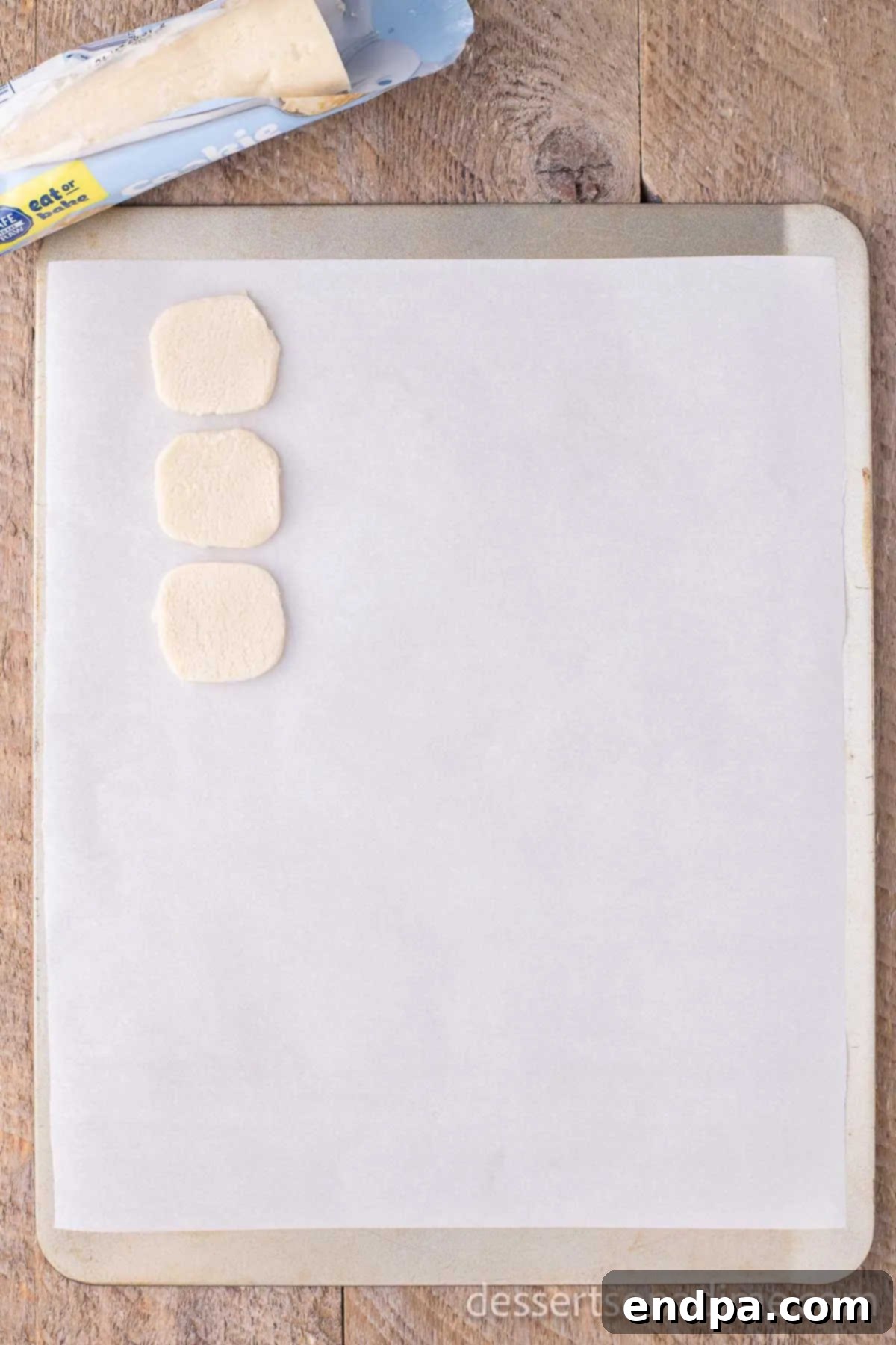 Whip Up Adorable Snowman Cookies 3 Individual portions of sugar cookie dough placed on a baking sheet lined with parchment paper, spaced for baking.