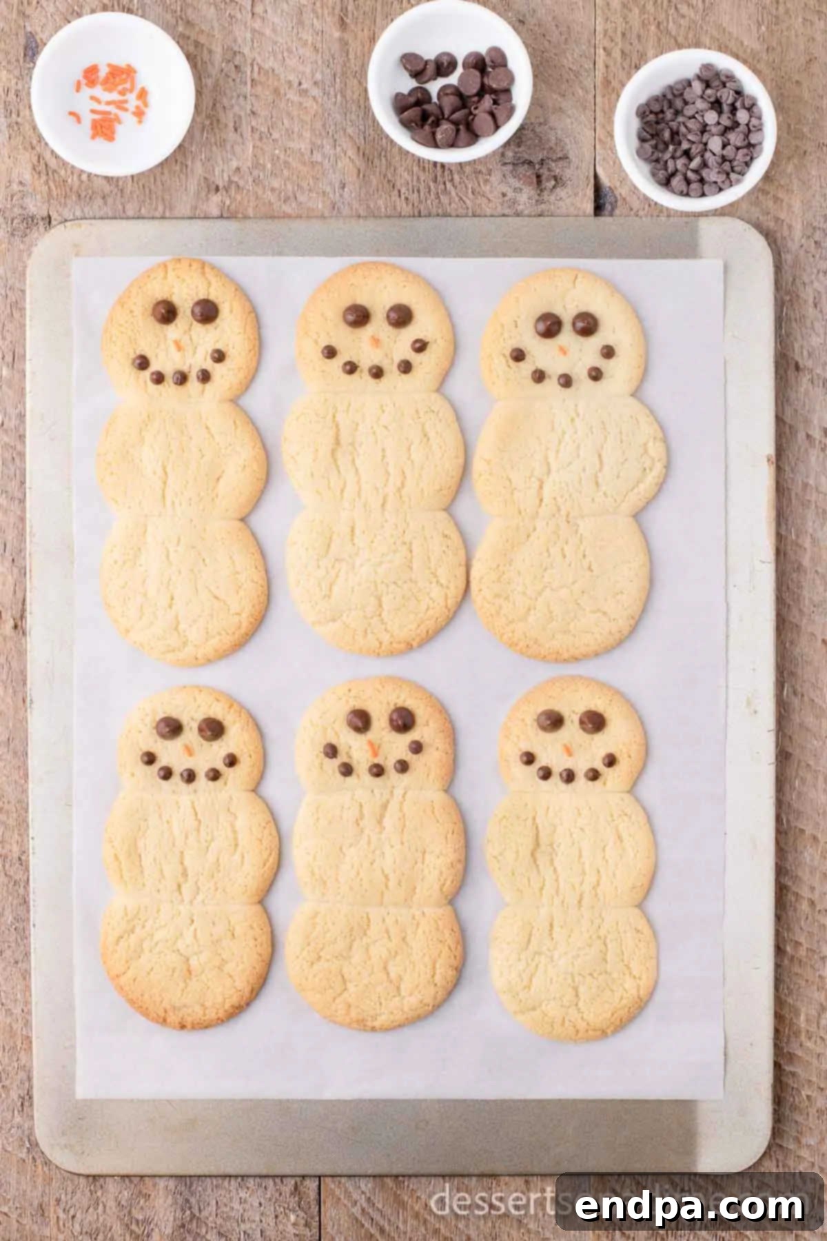 Whip Up Adorable Snowman Cookies 6 A snowman cookie partially decorated with chocolate chips for eyes and mini chocolate chips for a mouth, on a cooling rack.