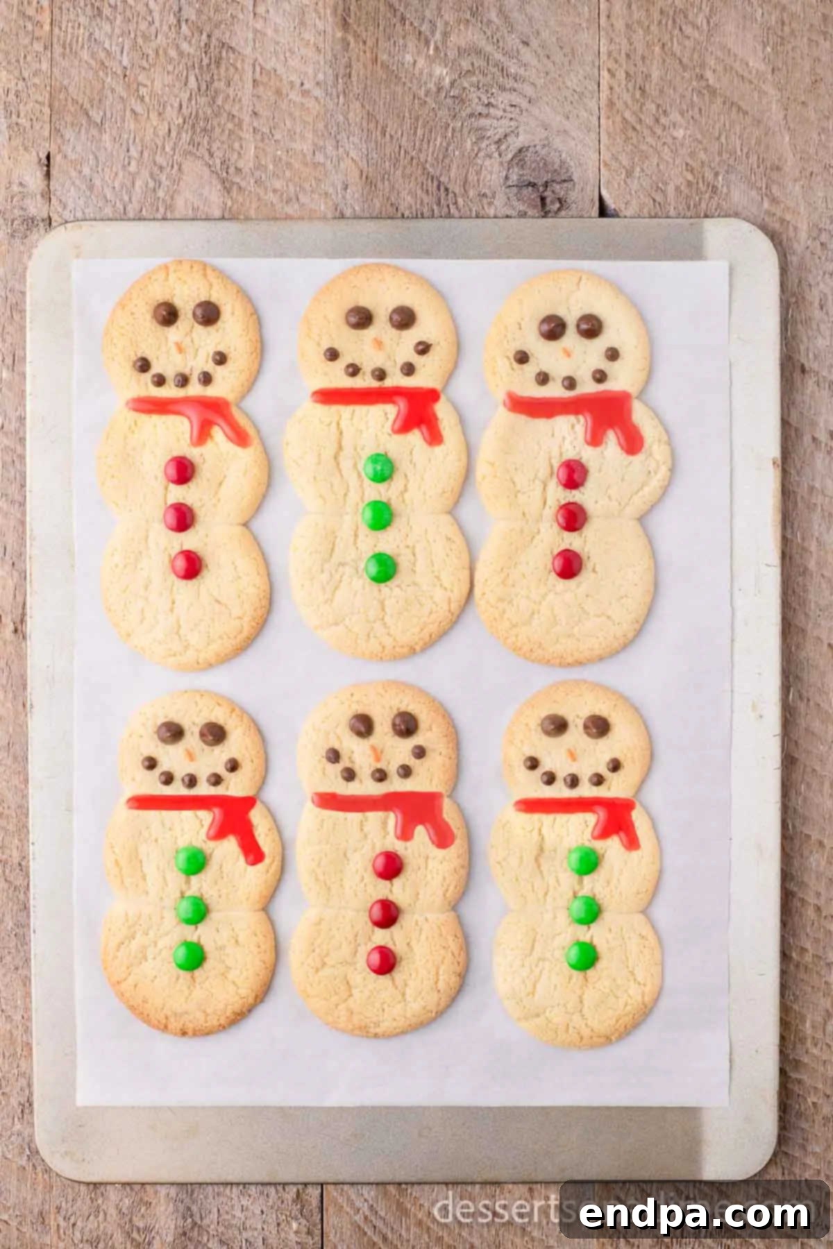 Whip Up Adorable Snowman Cookies 8 Completed snowman cookies featuring candy decorations and colorful icing scarves on a baking sheet.
