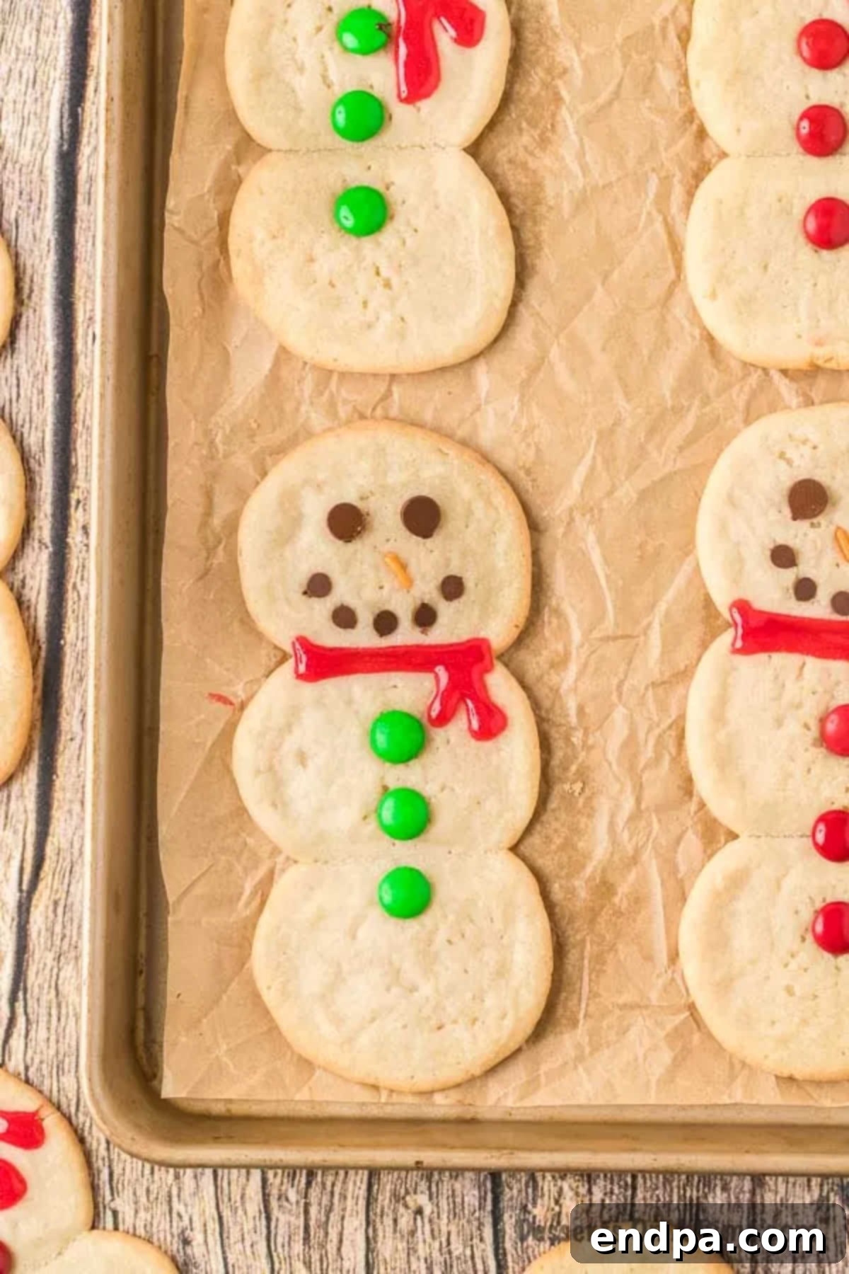 Whip Up Adorable Snowman Cookies 9 A close-up of a perfectly decorated snowman cookie with a red scarf, chocolate chip eyes, and M&M buttons, resting on a baking sheet.