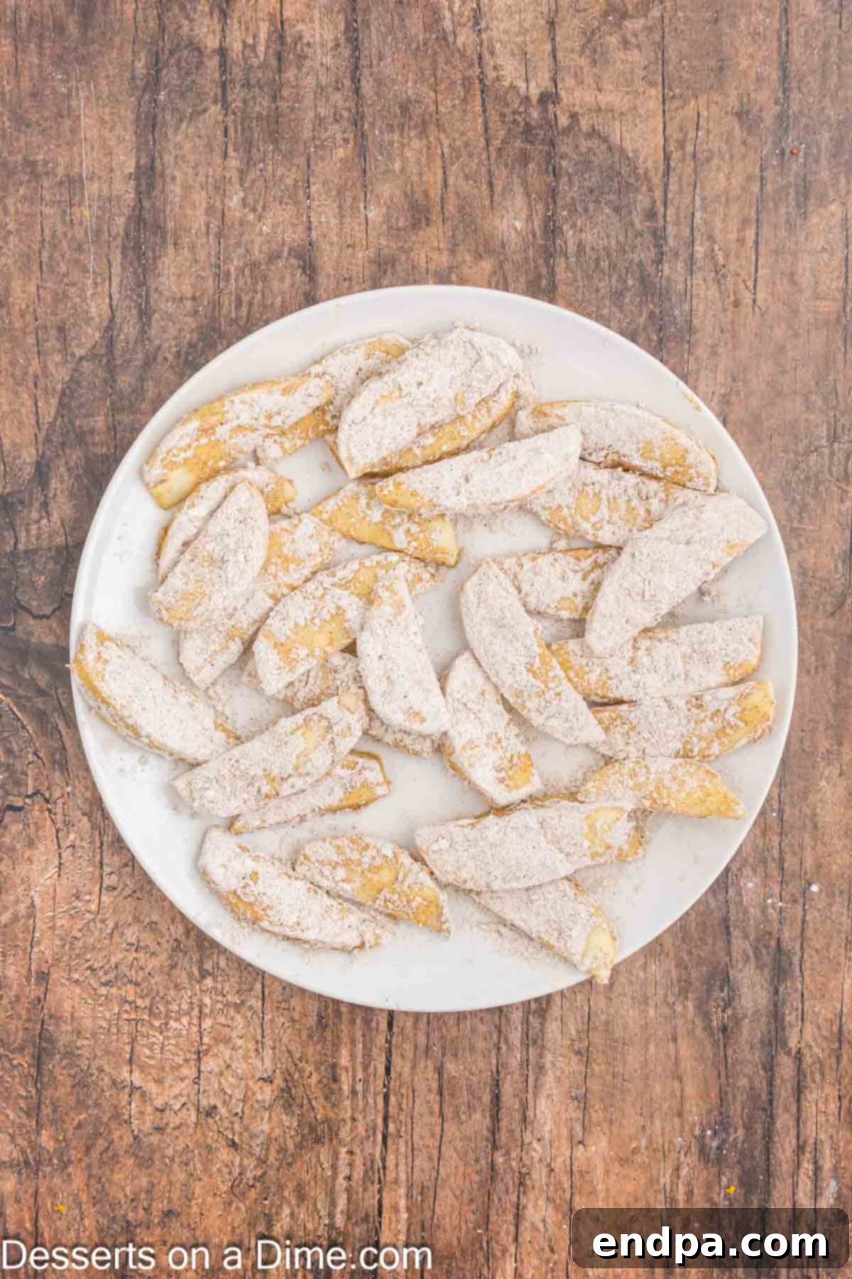 Apple slices dipped in coating and on a plate ready to be placed in the air fryer. 