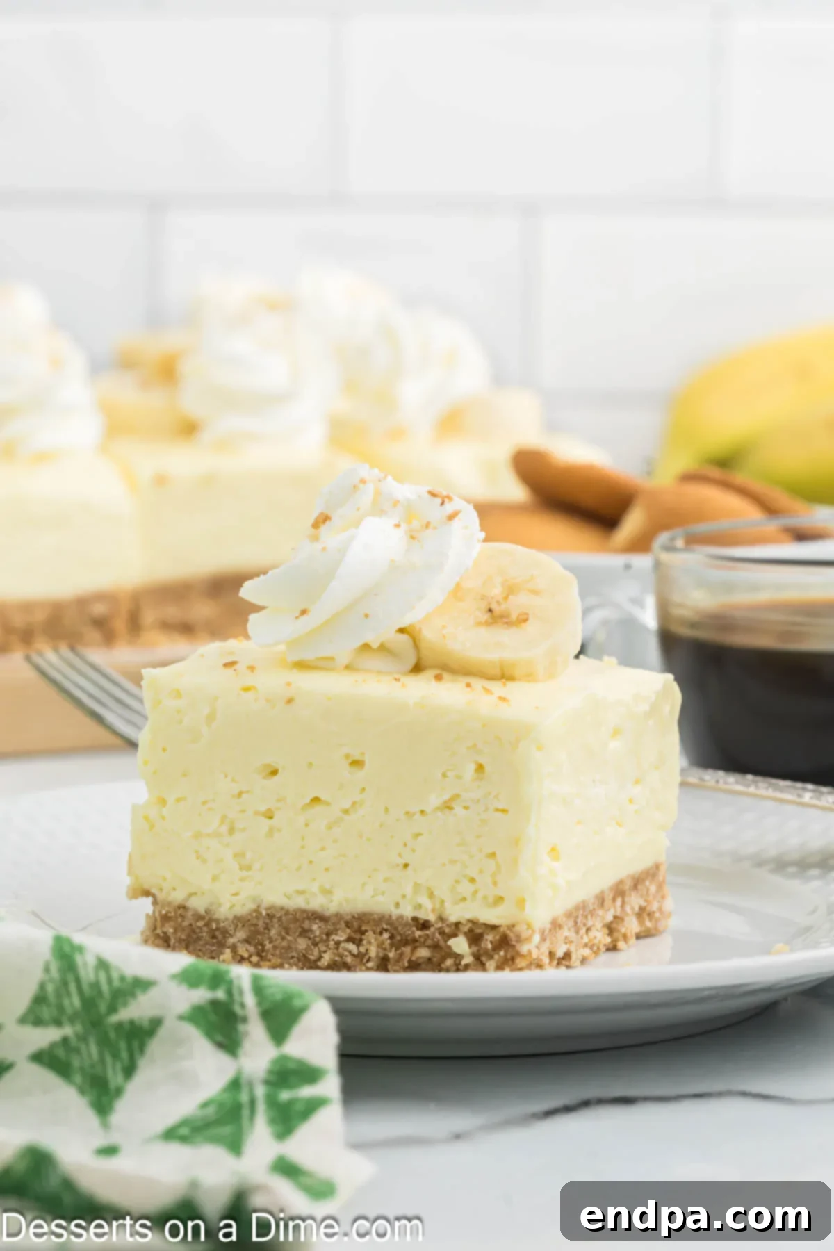 Dreamy Banana Cheesecake Bars 2 A slice of Banana Cream Cheesecake Bar on a white plate, topped with whipped cream and fresh banana slices.