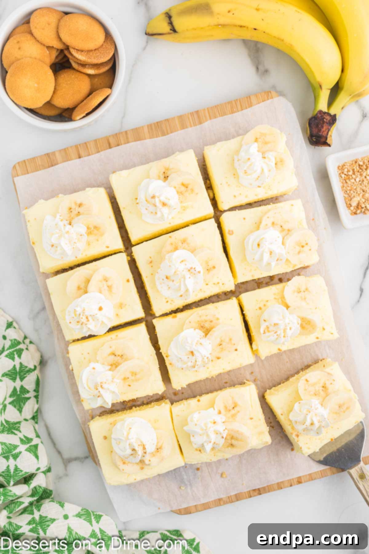 Dreamy Banana Cheesecake Bars 11 Individual Banana Cream Cheesecake Bars, topped with a dollop of whipped cream and a banana slice, presented on a platter.