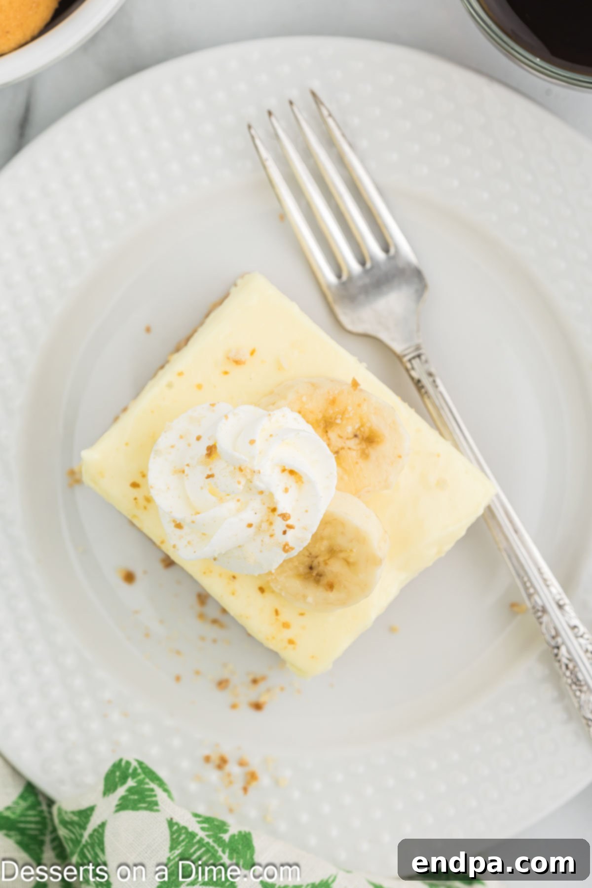 Dreamy Banana Cheesecake Bars 12 Several Banana Cream Cheesecake Bars cut into perfect squares, arranged on a white plate, showcasing their creamy layers.