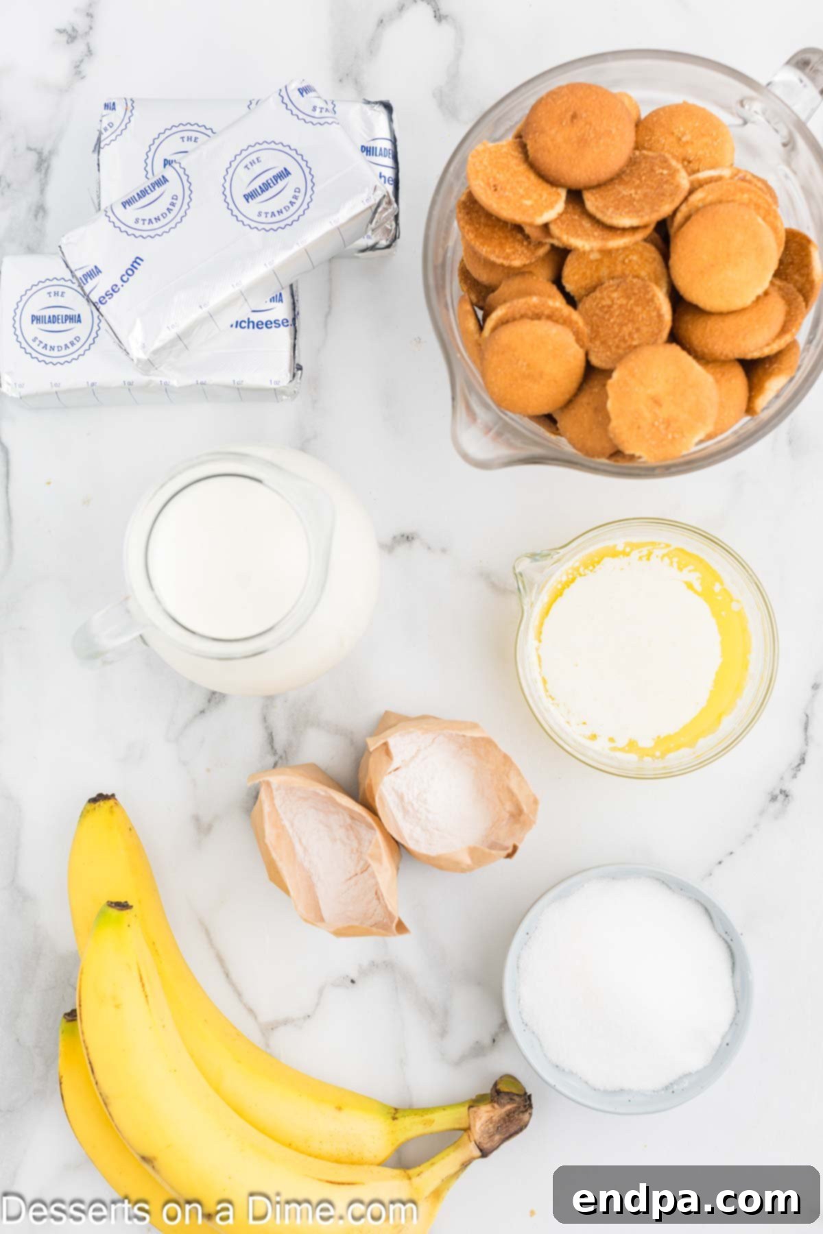 Dreamy Banana Cheesecake Bars 3 A flat lay of ingredients for Banana Cream Cheesecake Bars, including vanilla wafers, butter, heavy cream, sugar, cream cheese, instant banana pudding mix, and a fresh banana, alongside a container of whipped topping.