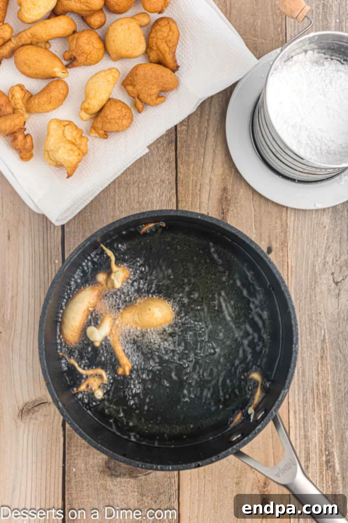 Hot vegetable oil bubbling in a deep pan on the stove, with spoonfuls of funnel cake batter being carefully dropped into it to fry.