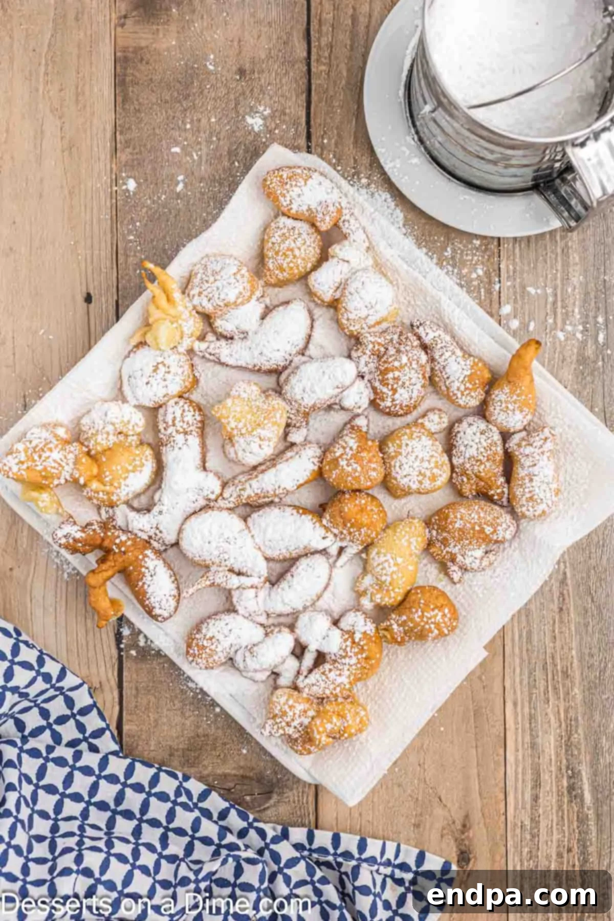 A freshly fried funnel cake bite sitting on a plate lined with paper towels, generously covered in a thick layer of powdered sugar.